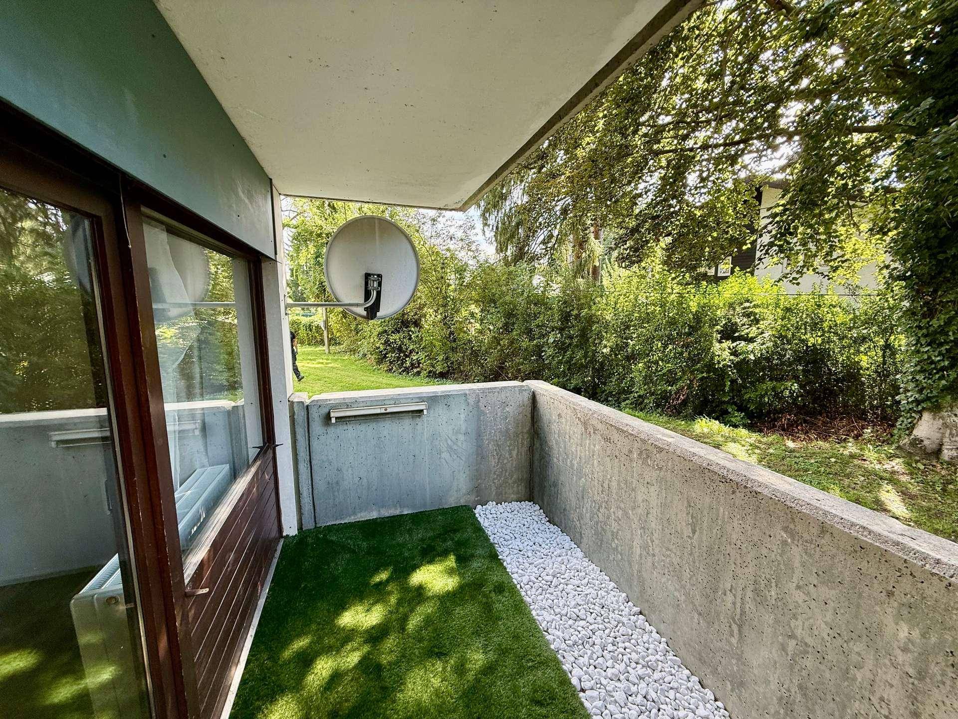 Kleiner Balkon mit Kunstrasen, Zierkies und Blick ins Grüne.