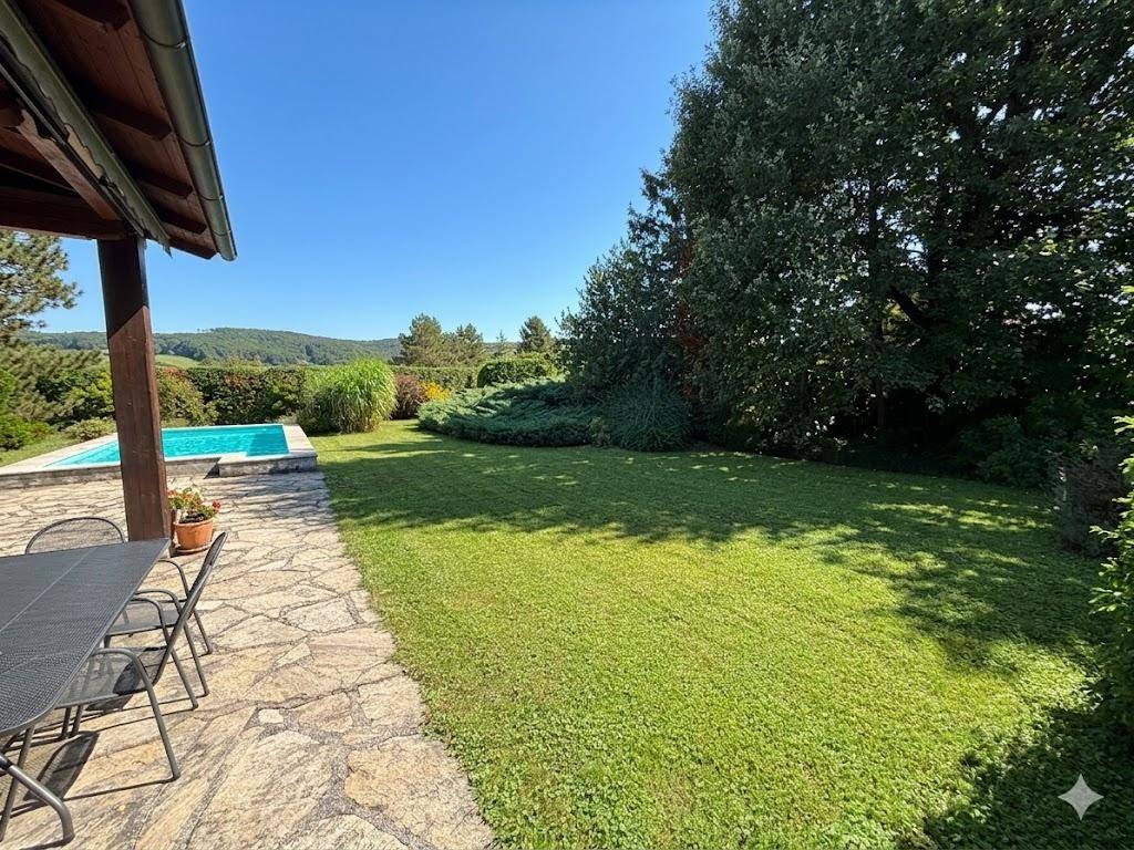 Terrasse und weitläufiger Garten mit Rasenfläche und Fernblick auf die Hügellandschaft.