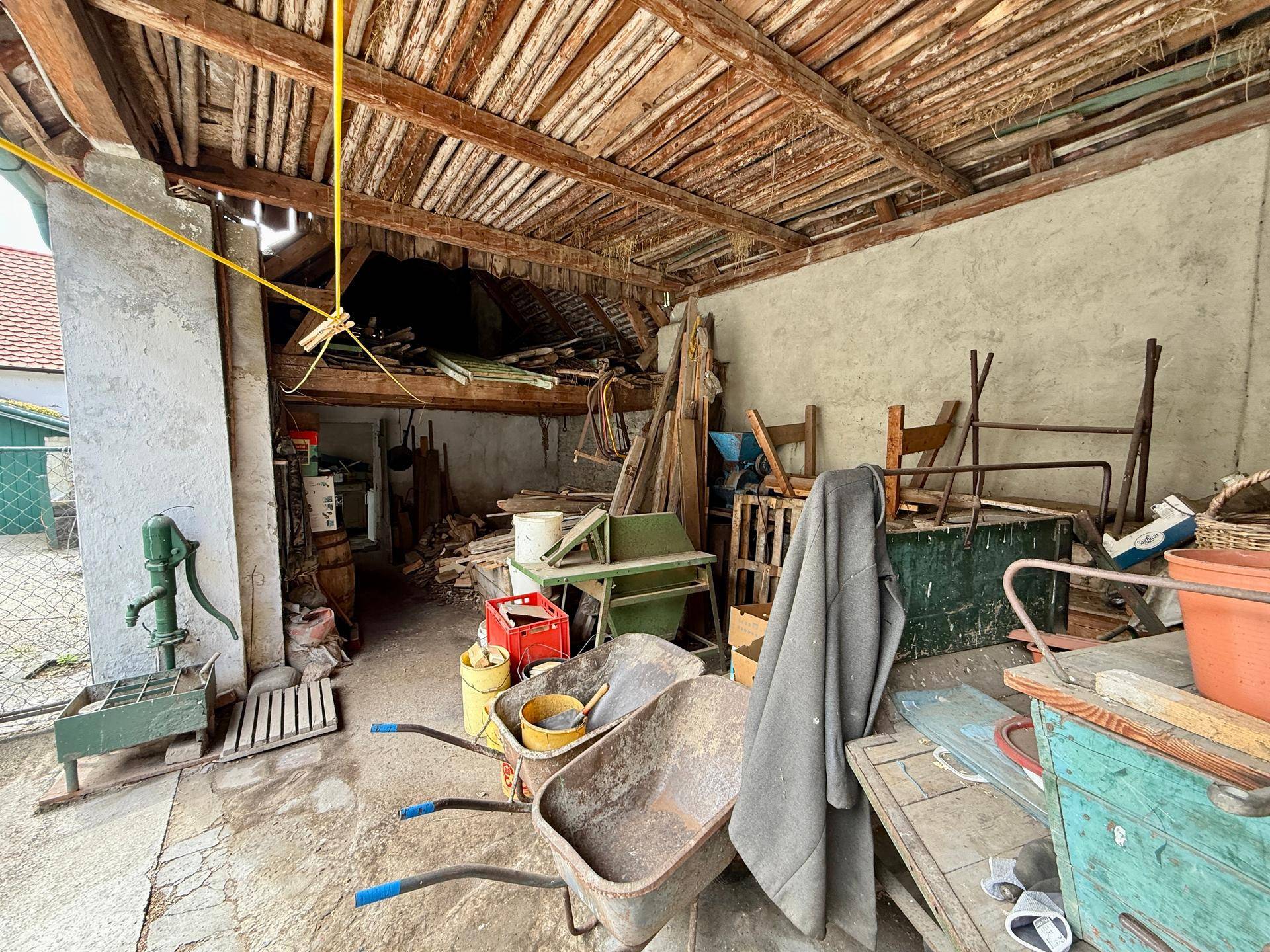 Überdachter Außenbereich mit sichtbarer Holzkonstruktion und gelagerten Geräten.