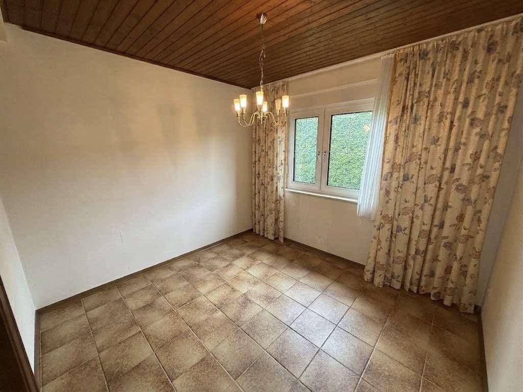Schlafzimmer mit Fliesenboden, großen Fenstern und floral gemusterten Vorhängen.