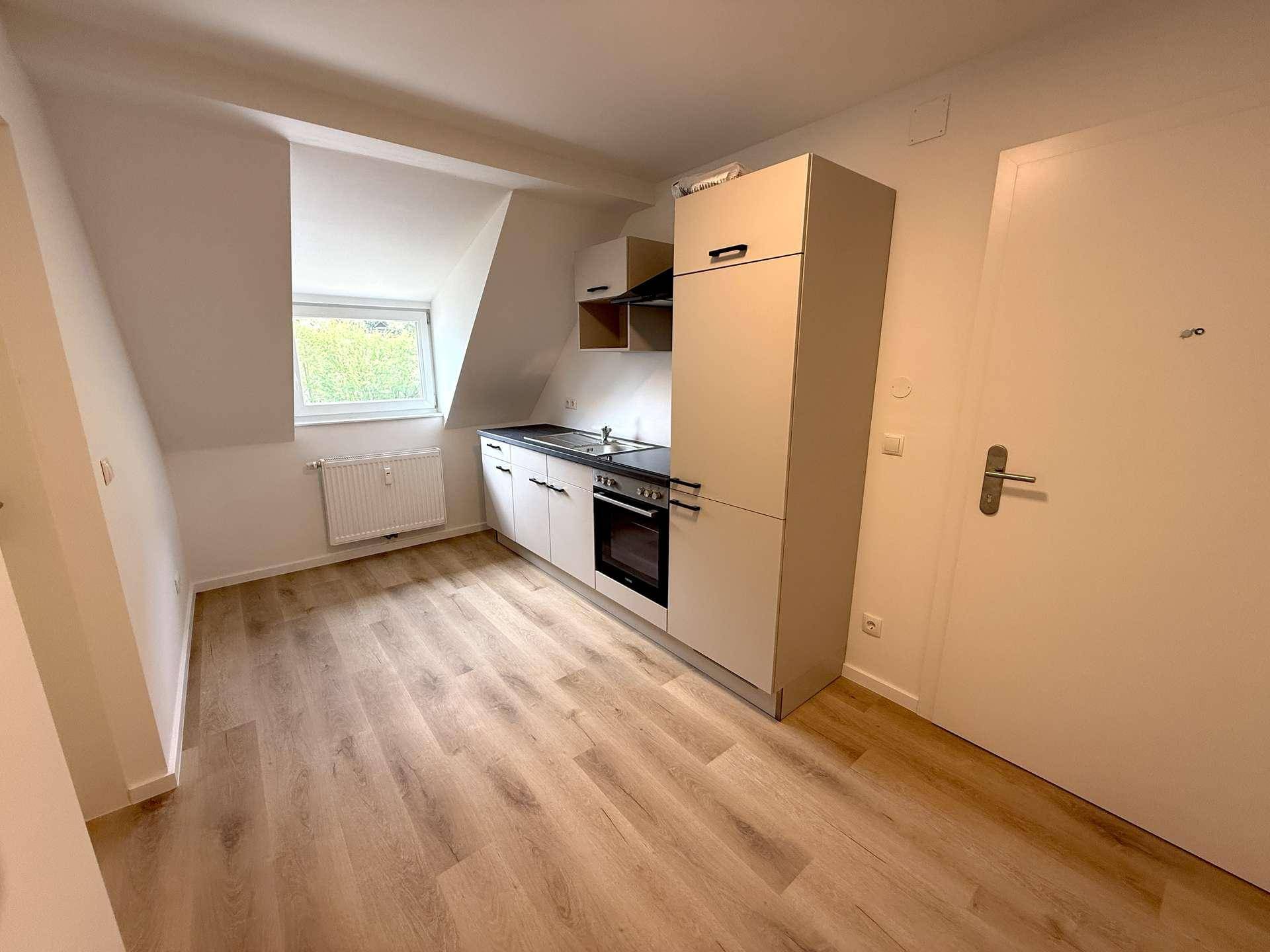 Heller Raum mit Küchenzeile, Laminatboden und Dachschräge, ideal für ein Studio-Apartment.