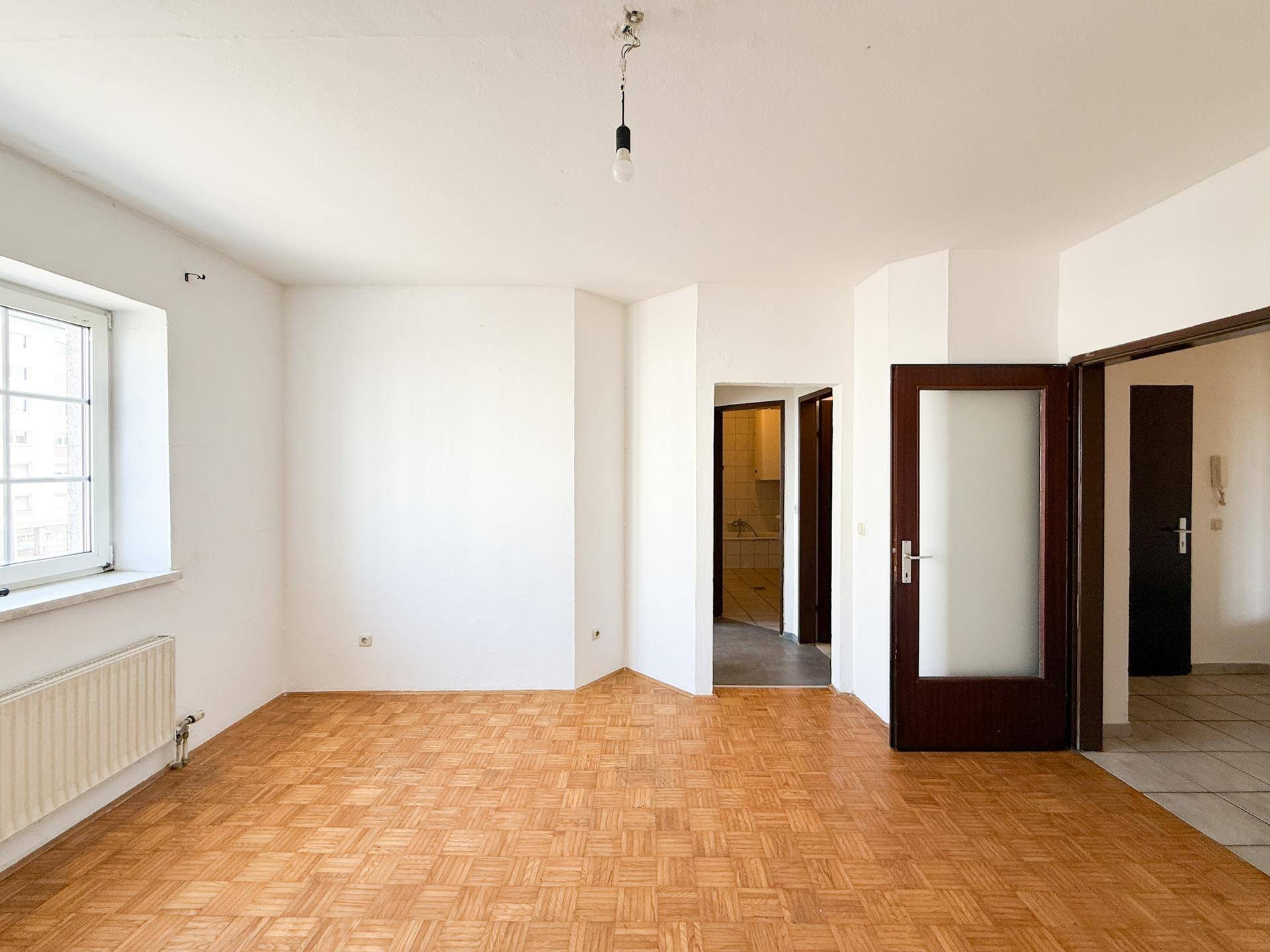 Geräumiges Wohnzimmer mit Parkettboden und mehreren Türen, die zu angrenzenden Bereichen führen.