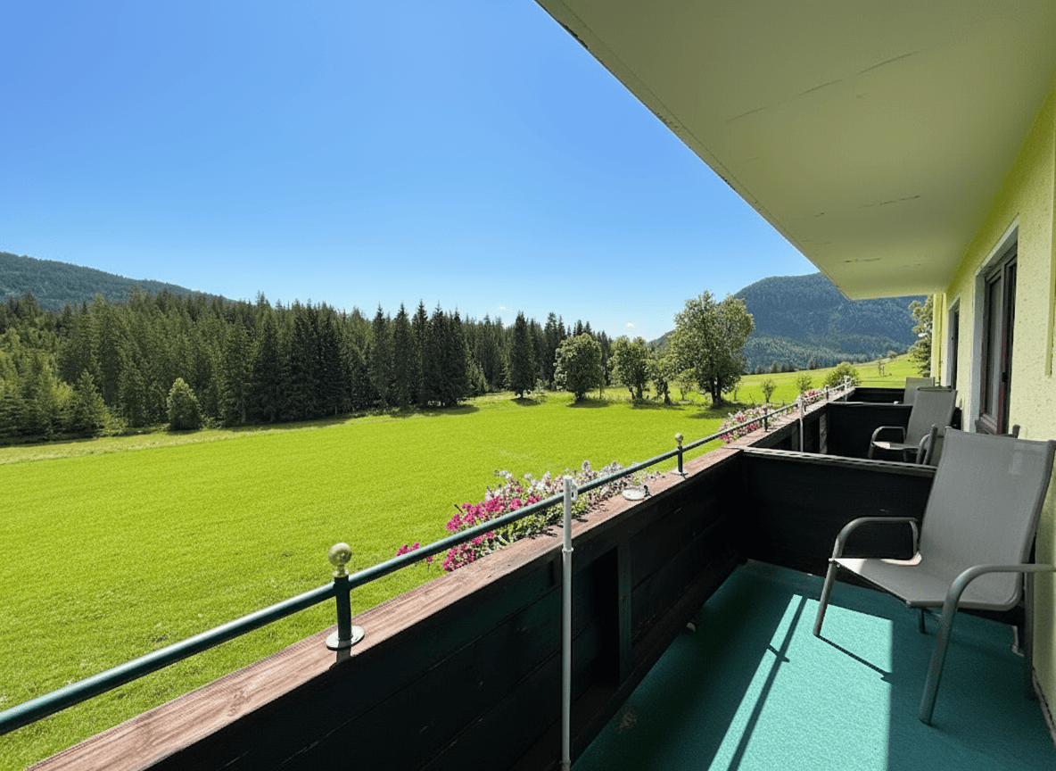 Geräumiger Balkon mit Holzboden und Metallgeländer, bietet einen weiten Blick auf grüne Wiesen und bewaldete Berge.