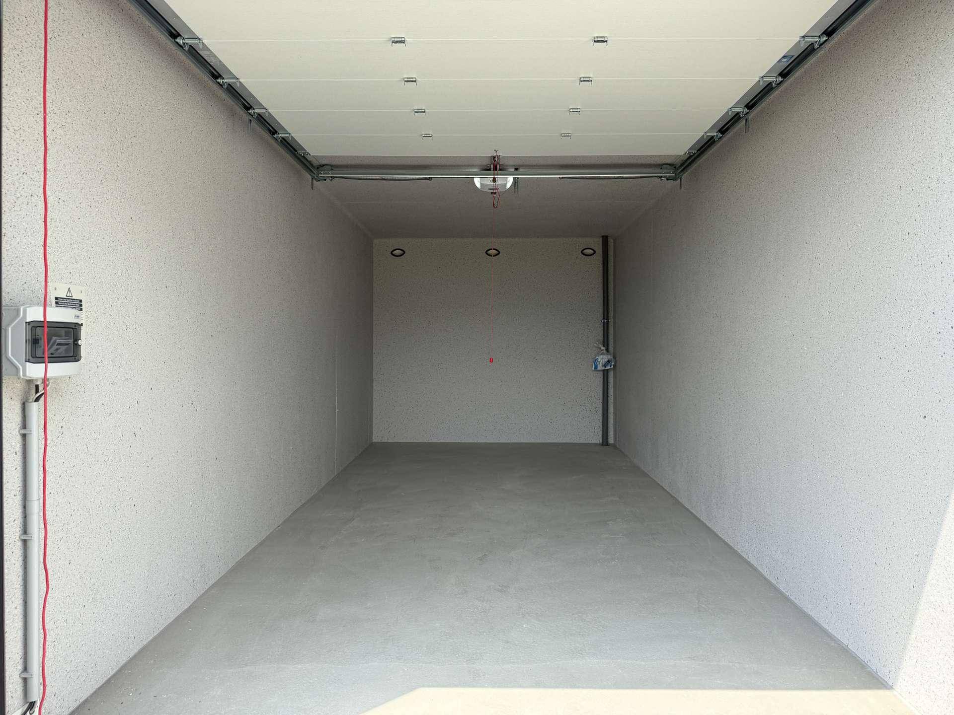 Leere, saubere Garagenbox mit glattem Betonboden und elektrischem Anschluss an der Wand.