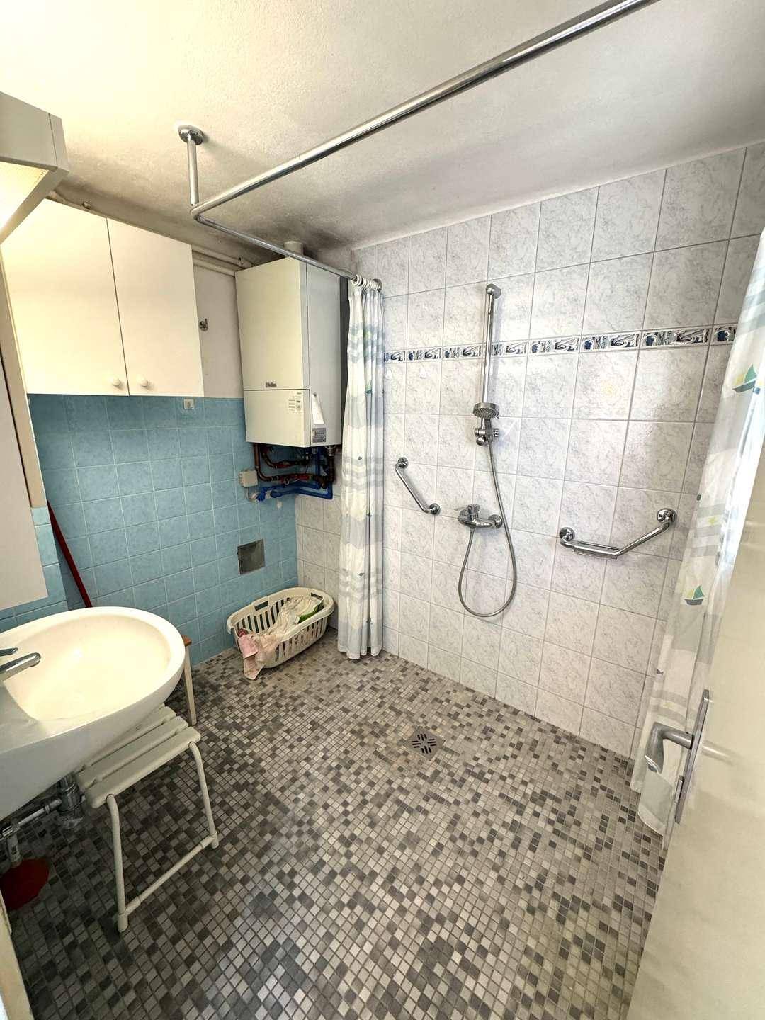Badezimmer mit ebenerdiger Dusche, Fliesenboden und Wandheizung.