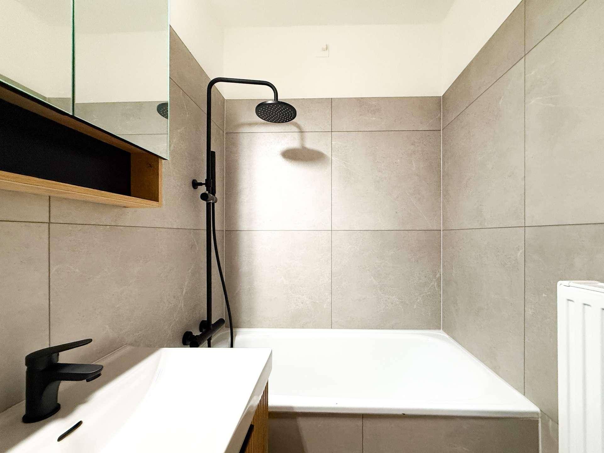 Badewanne mit moderner schwarzer Regendusche und hellgrauen Wandfliesen im Badezimmer.