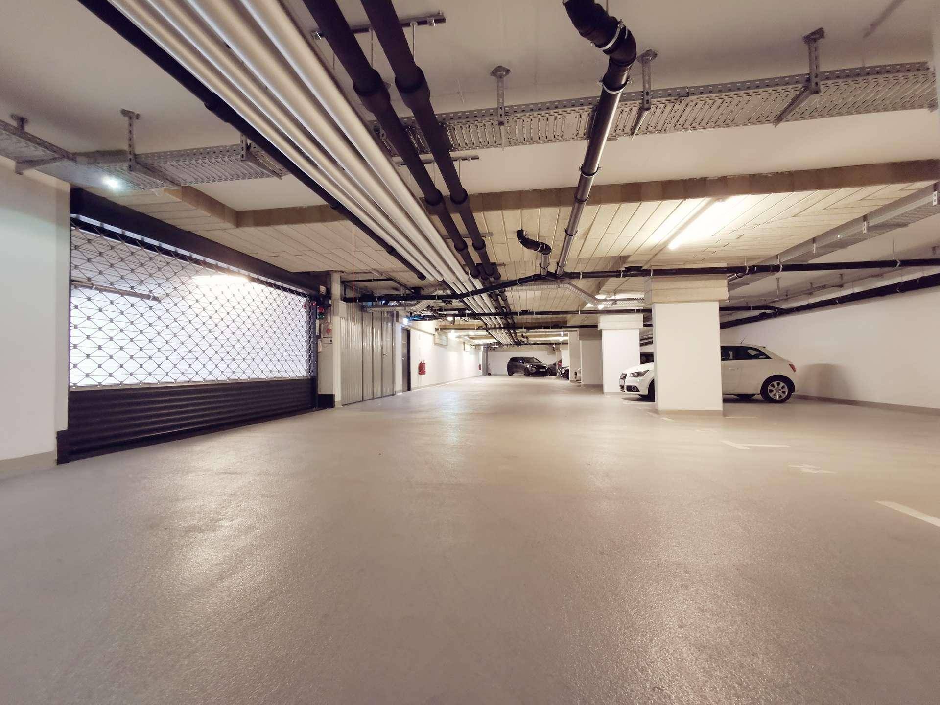 Geräumige Tiefgarage mit Betonboden und sichtbaren Installationen an der Decke.