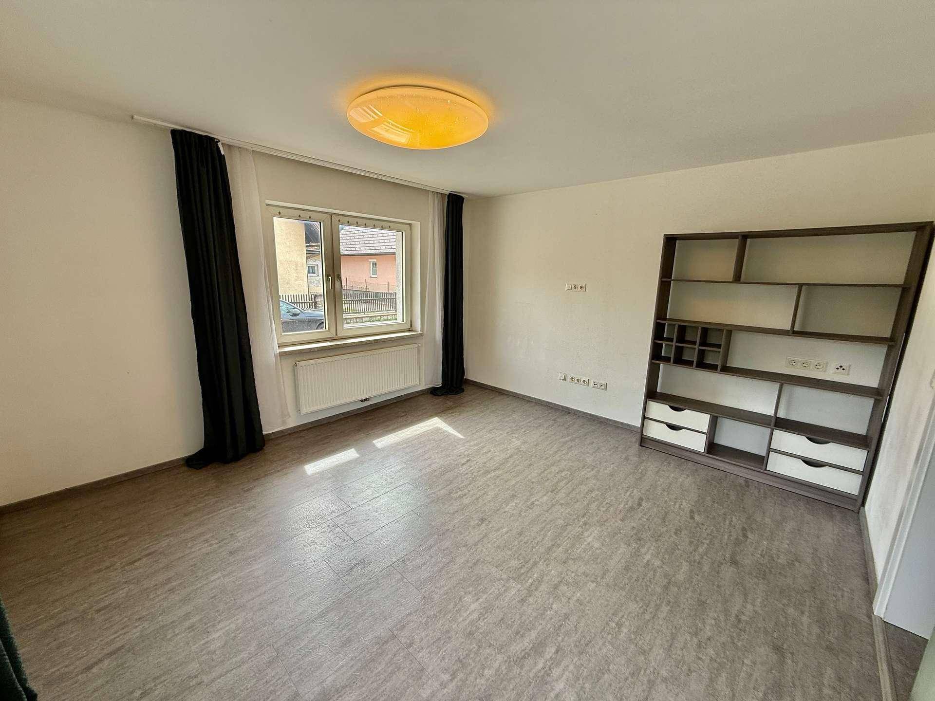 Helles Zimmer mit Laminatboden, großem Fenster und einem Regal, bereit zur individuellen Gestaltung.