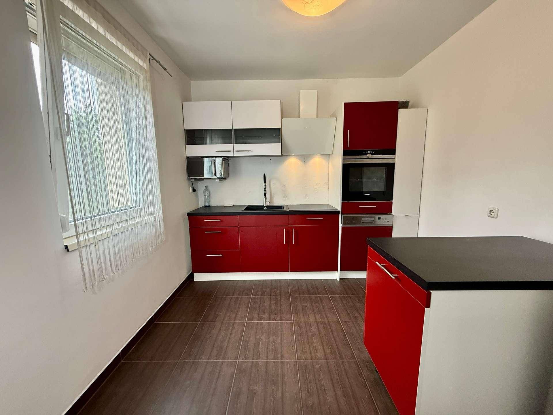 Moderne Küche mit roten Hochglanzfronten, integrierten Geräten und Fenster.