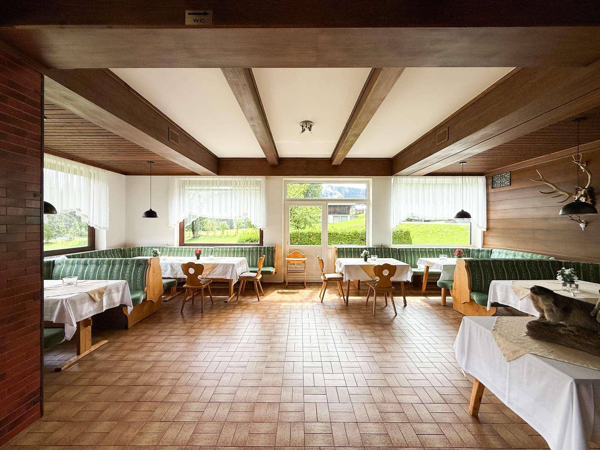 Geräumiger Speisesaal mit Holzbalken, gepolsterten Bänken und Blick auf die grüne Landschaft.