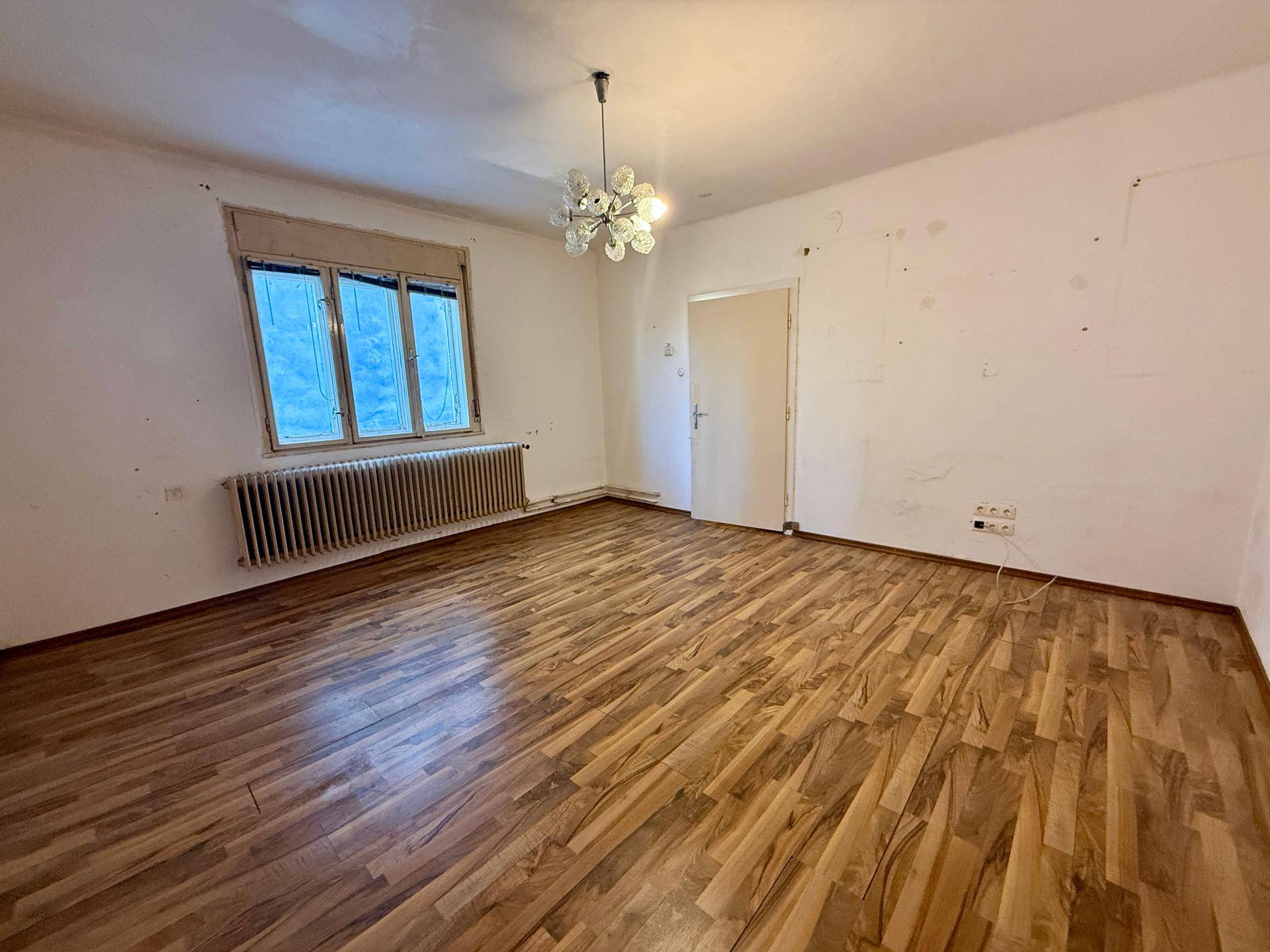 Geräumiges Wohnzimmer mit Laminatboden und großem Fenster, bereit zur Neugestaltung.