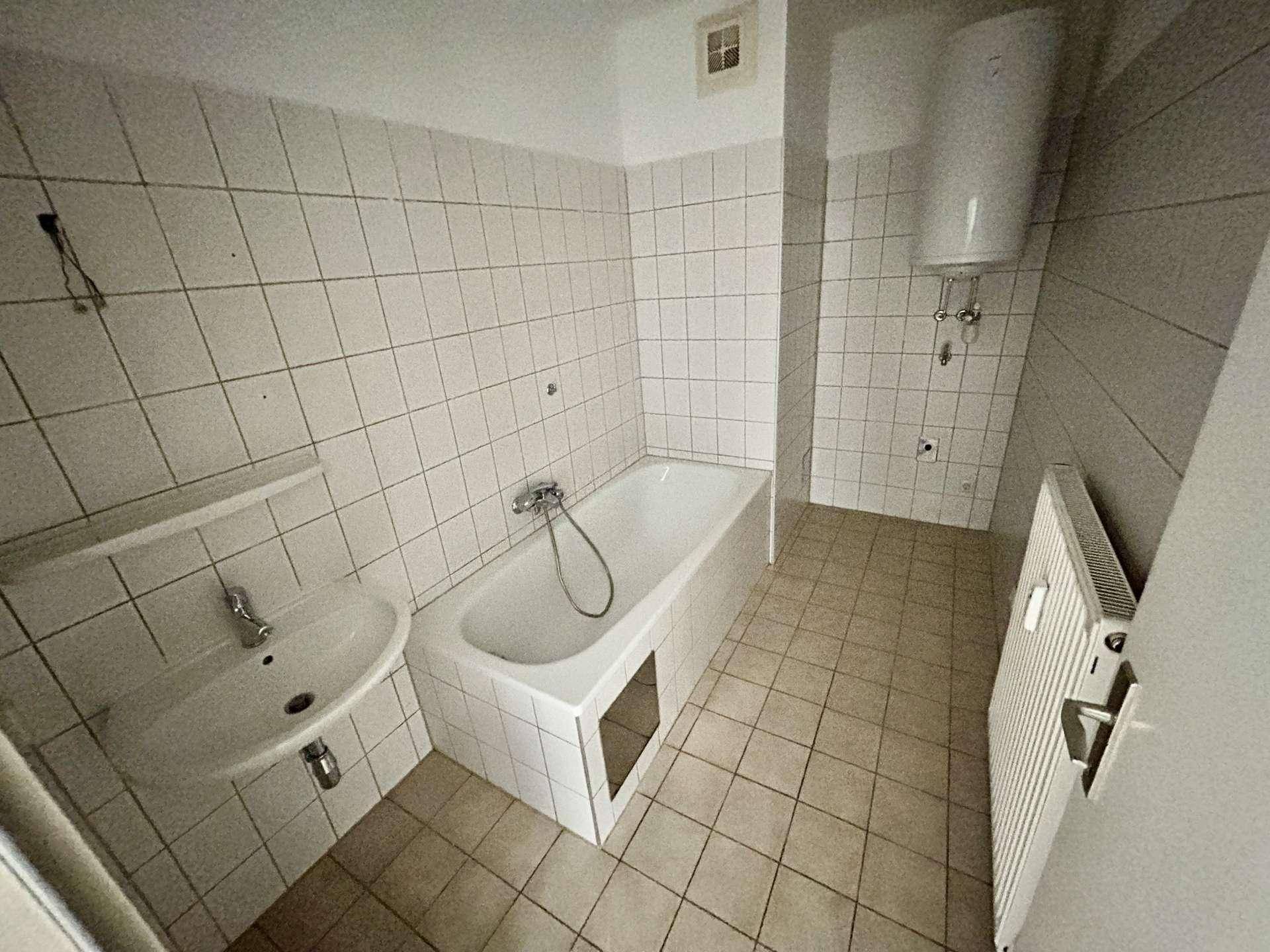Gefliestes Badezimmer mit Badewanne, Waschbecken und Boiler, in einem älteren Stil gehalten.
