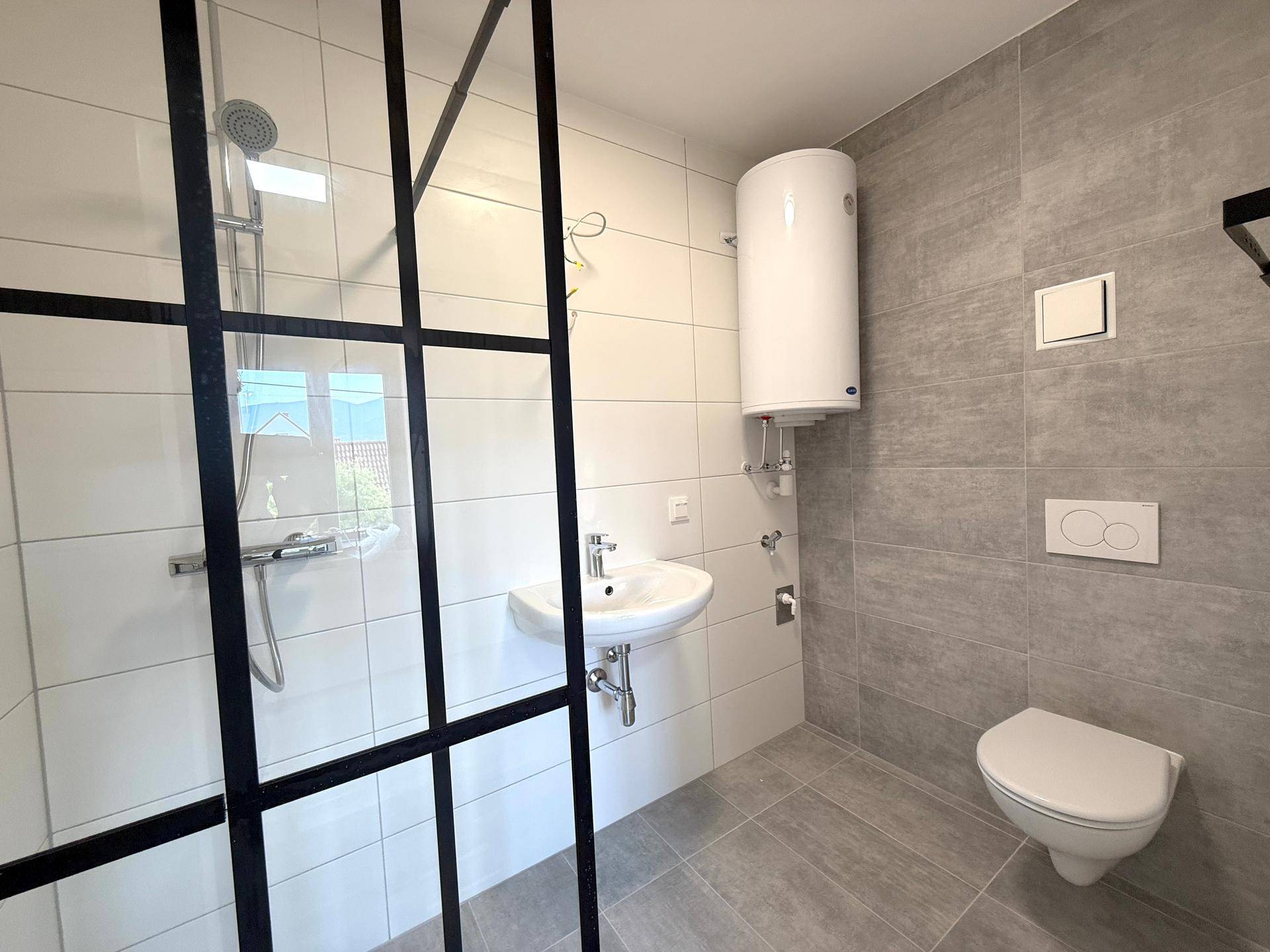 Modernes Badezimmer mit begehbarer Dusche, Hänge-WC, Waschbecken und Wandfliesen in Grau und Weiß.