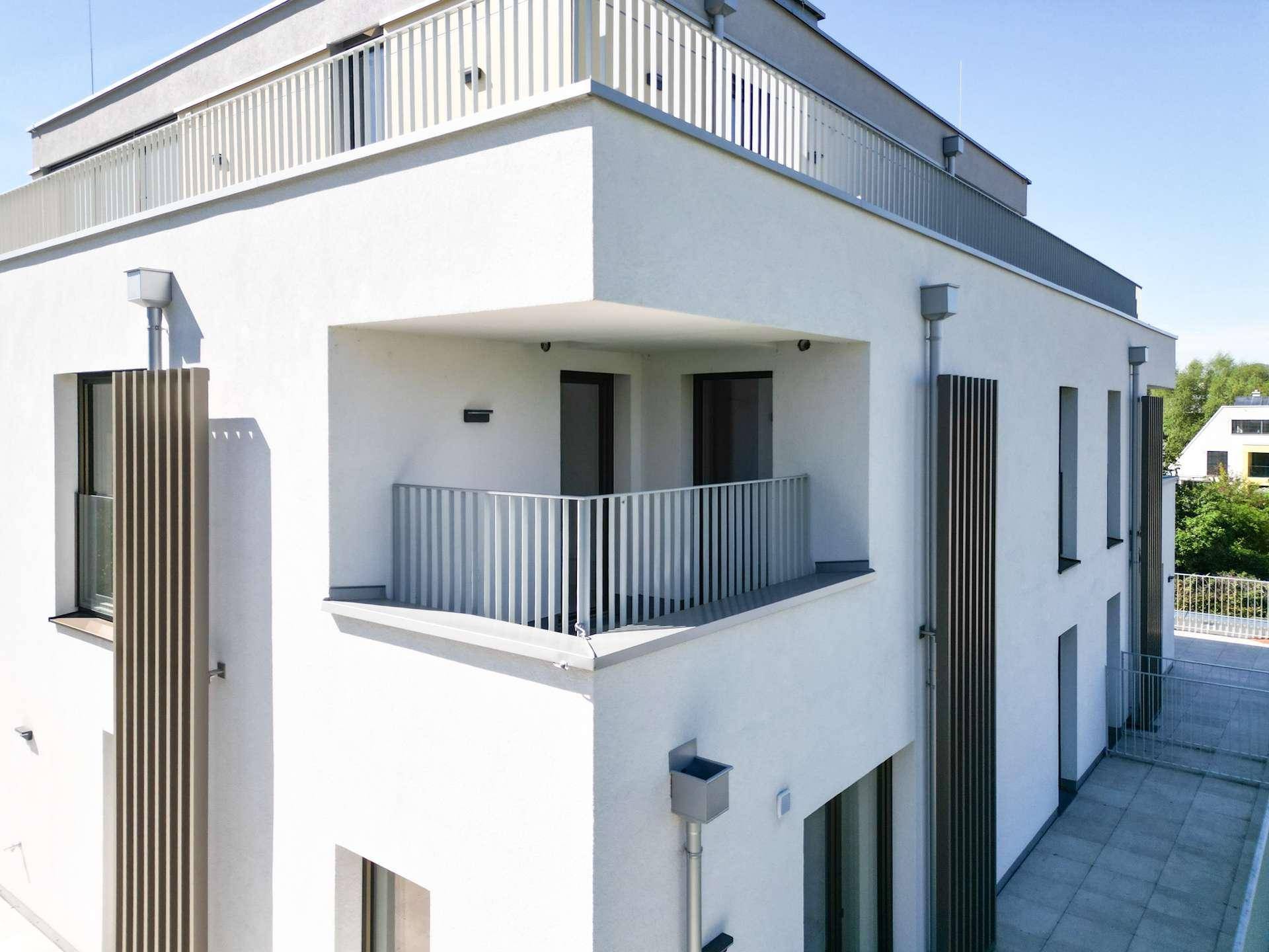 Moderne Gebäudefassade mit Balkonen, weißen Wänden und vertikalen Holzlamellen.