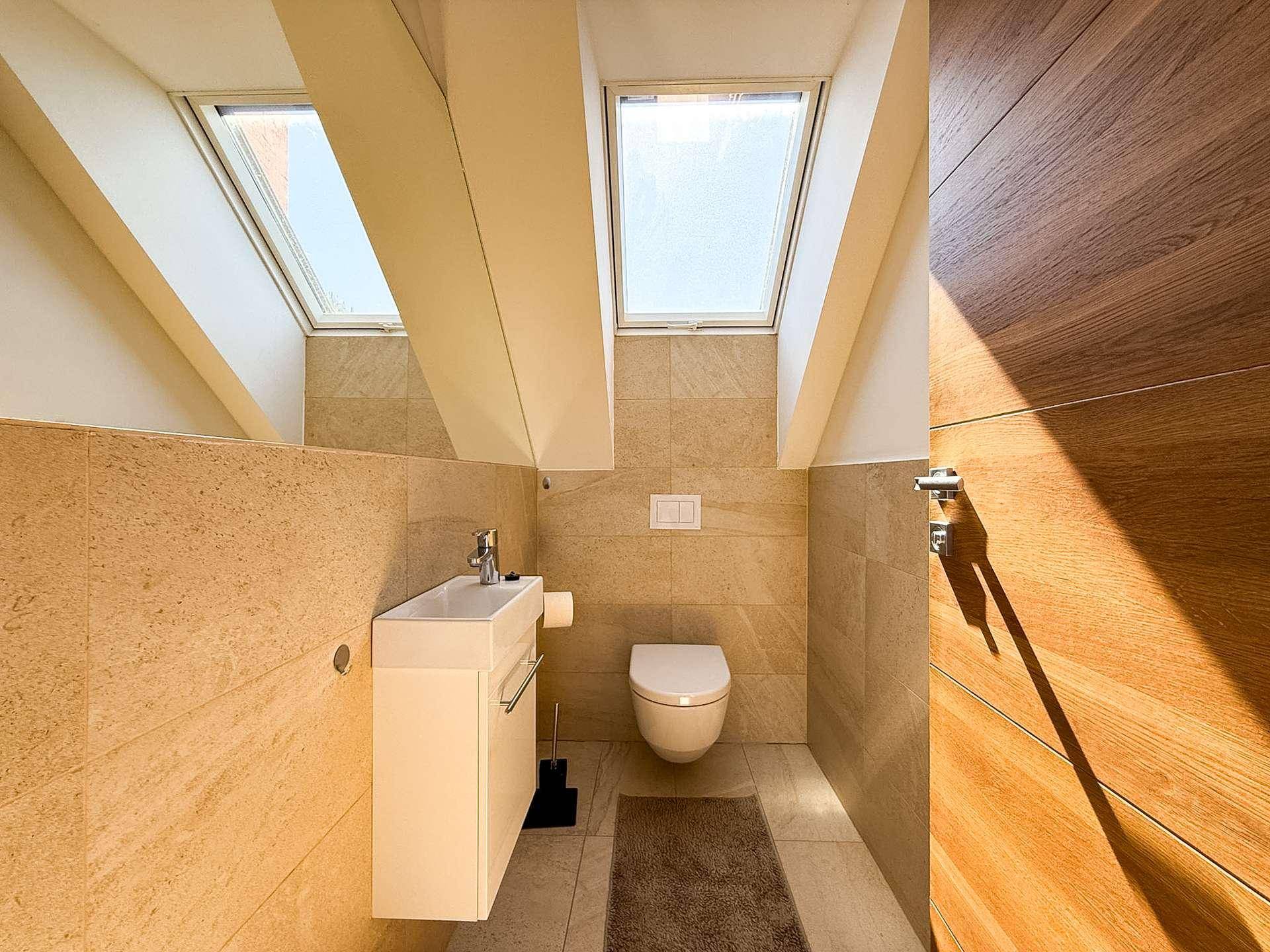 Modernes WC mit Dachfenstern, Wand-WC und schwebendem Waschtisch in hellen Fliesen.