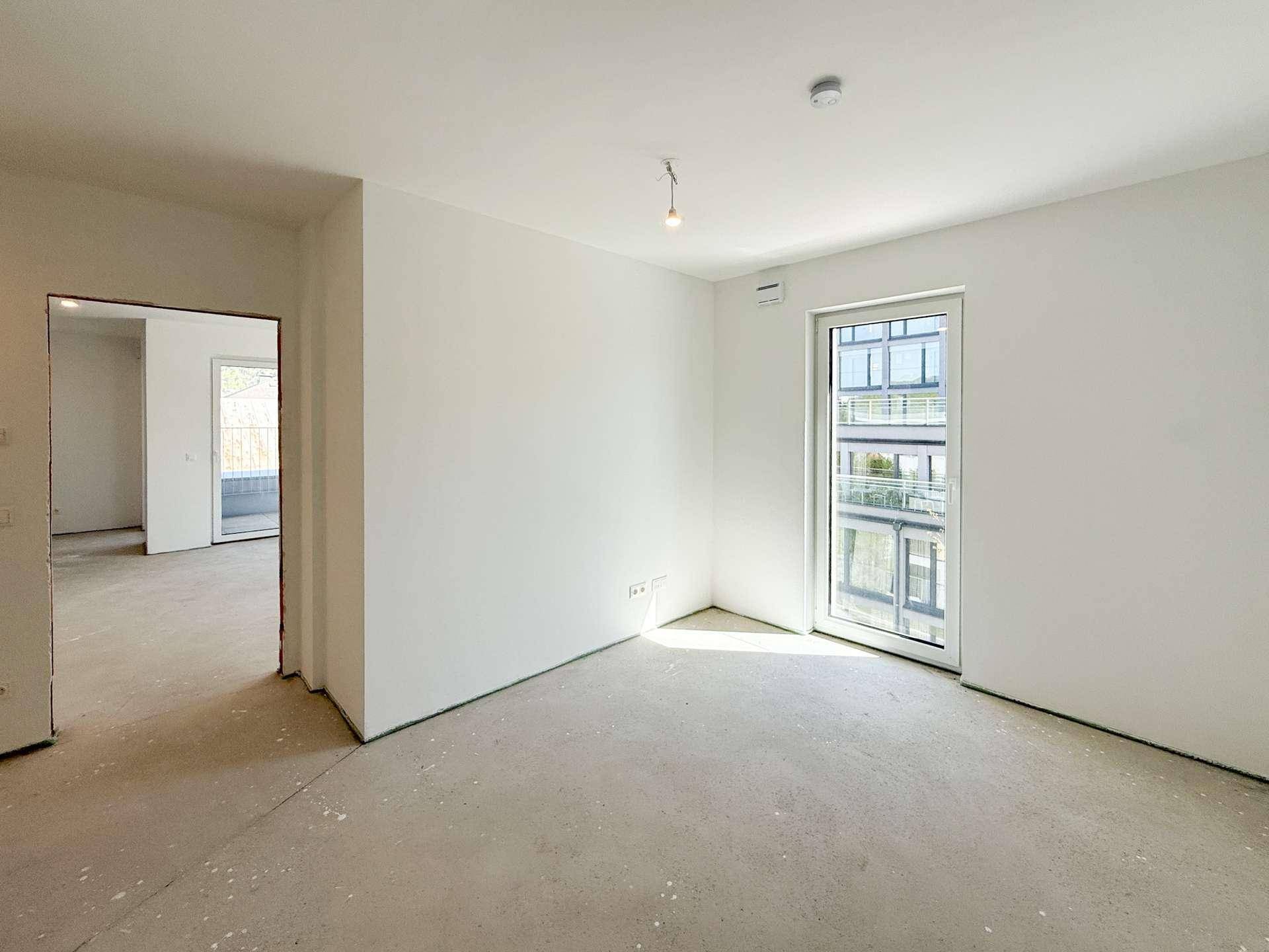 Unmöblierter Raum im Rohbau mit Fenster und viel Tageslicht.