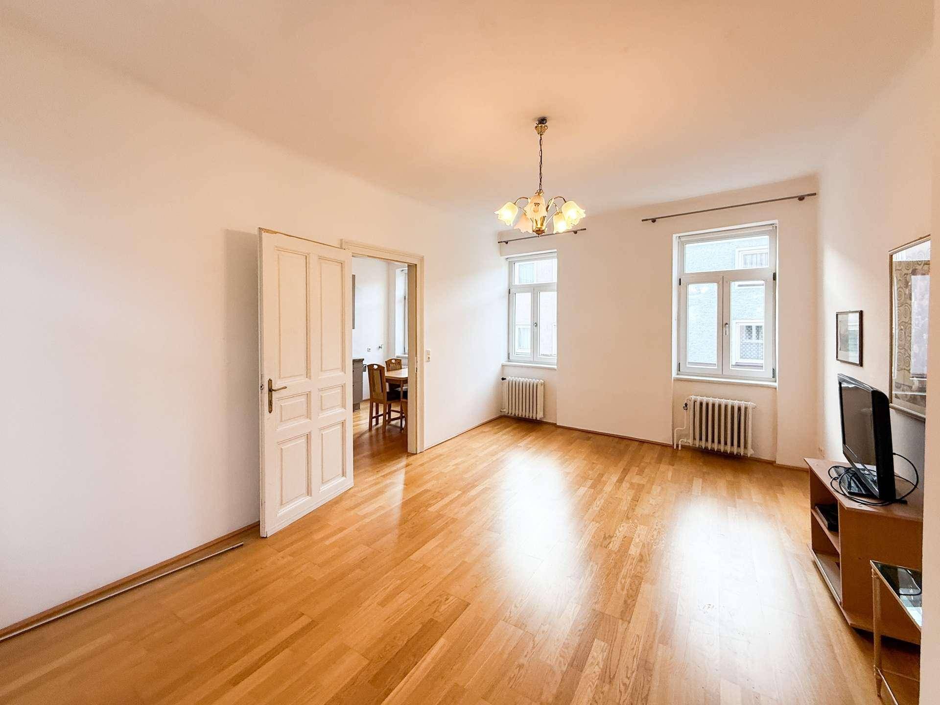 Großzügiges Wohnzimmer mit Parkettboden und hohen Fenstern, bietet eine angenehme Wohnatmosphäre.
