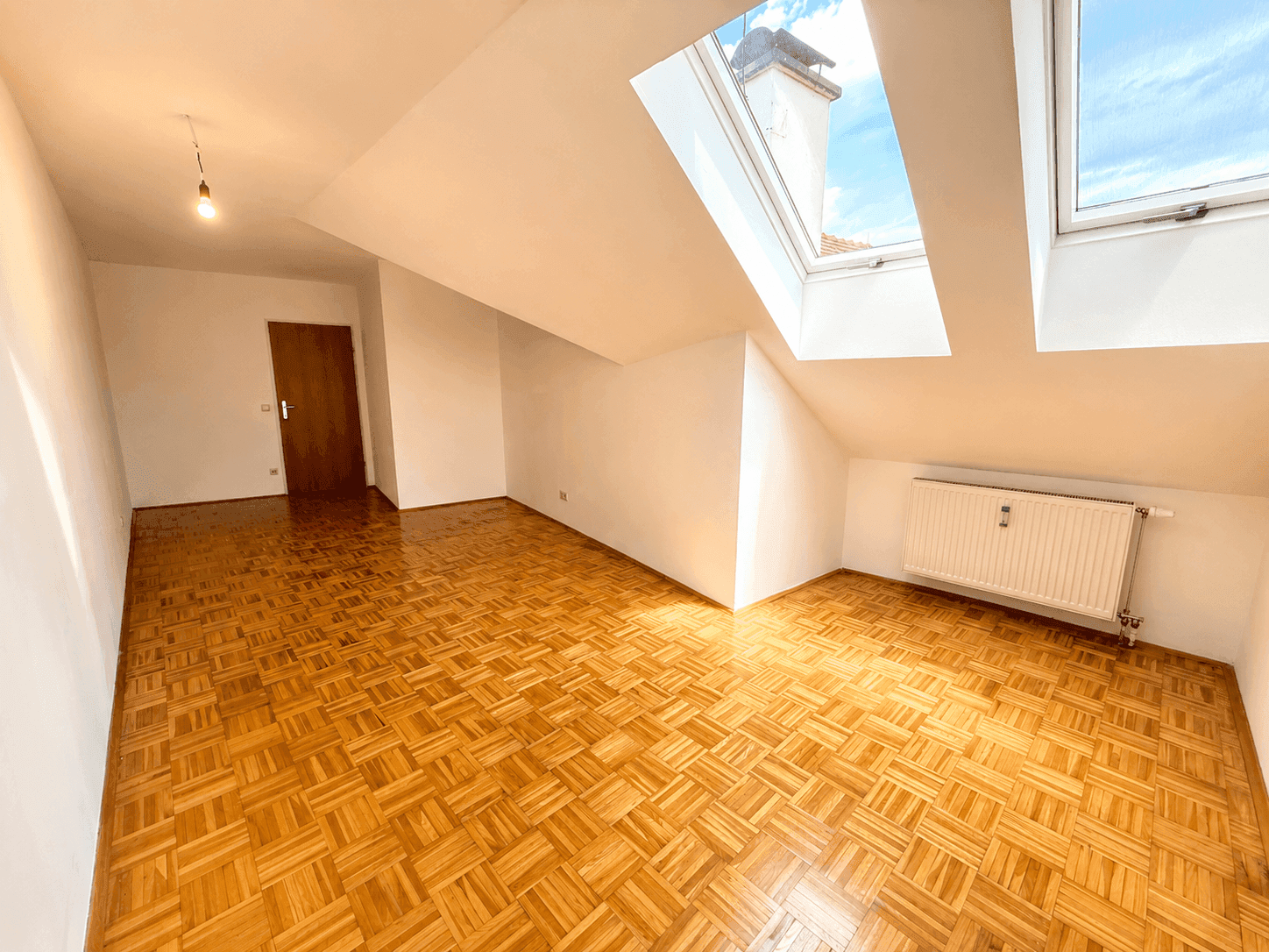 Helles Dachgeschosszimmer mit Parkettboden, Dachschrägen und zwei großen Dachfenstern.