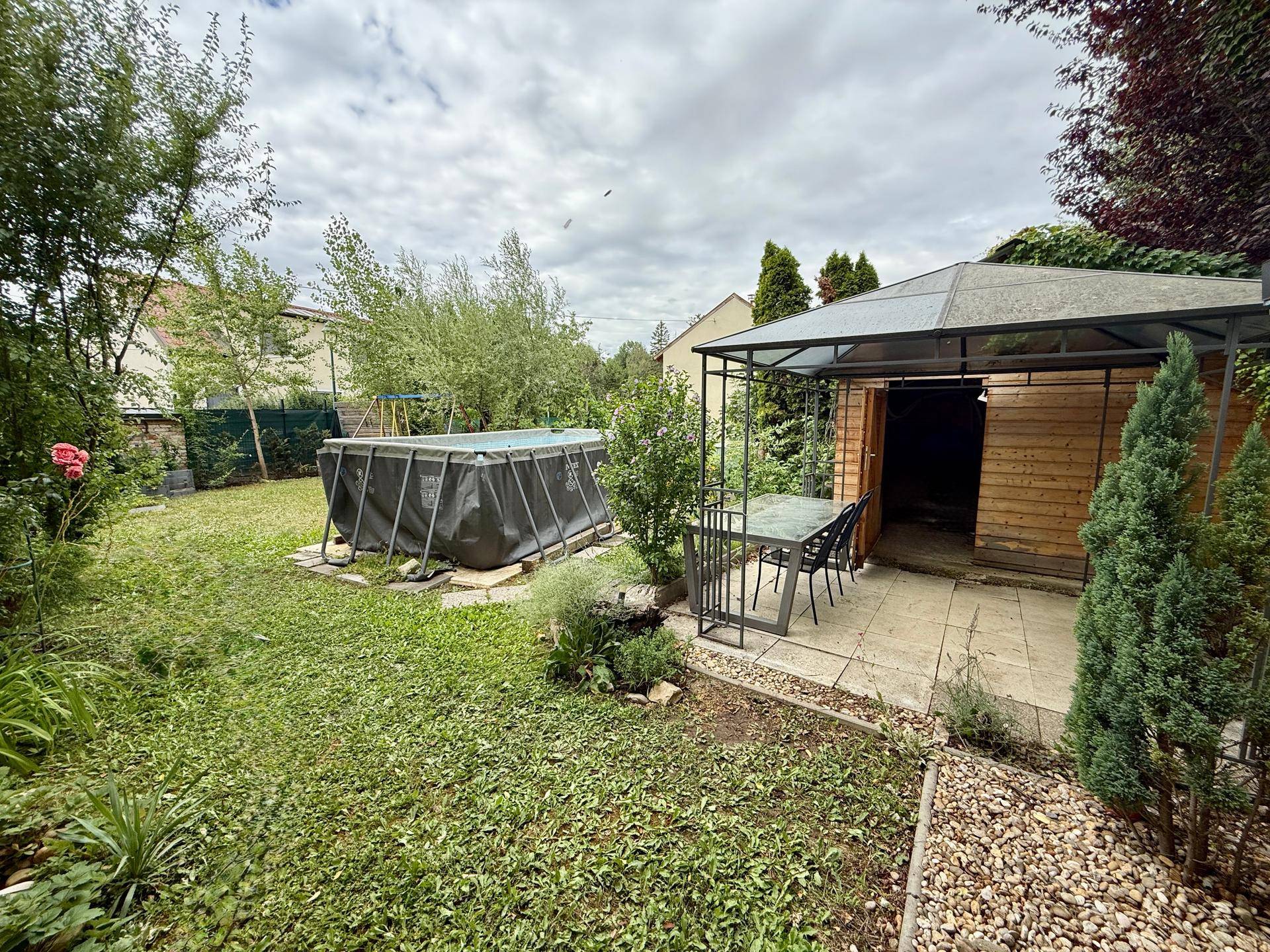 Gepflegter Garten mit überdachtem Sitzbereich, Aufstellpool und Gartenhaus.