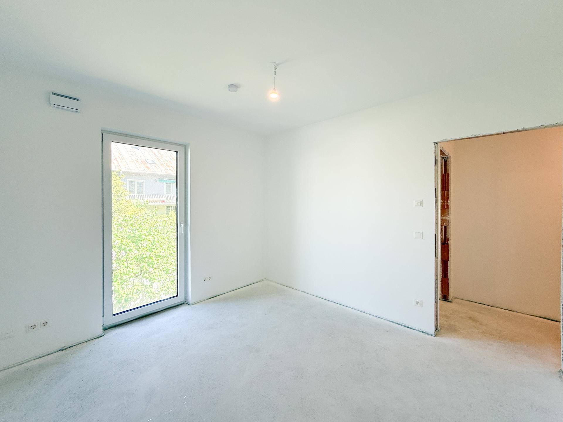Helles Schlafzimmer im Rohbau mit Fenster und vorbereiteten Anschlüssen.