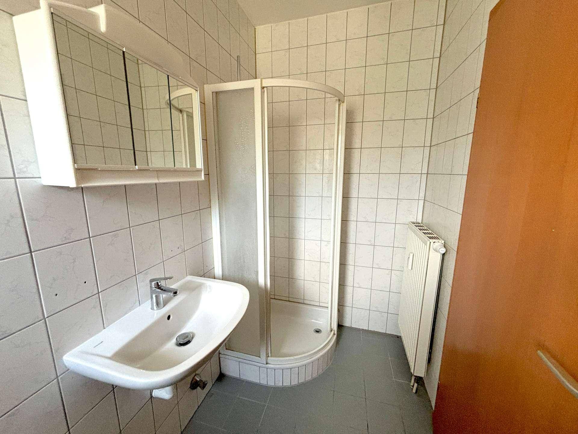 Badezimmer mit weiß gefliesten Wänden, einer Duschkabine, Waschbecken und Spiegelschrank.