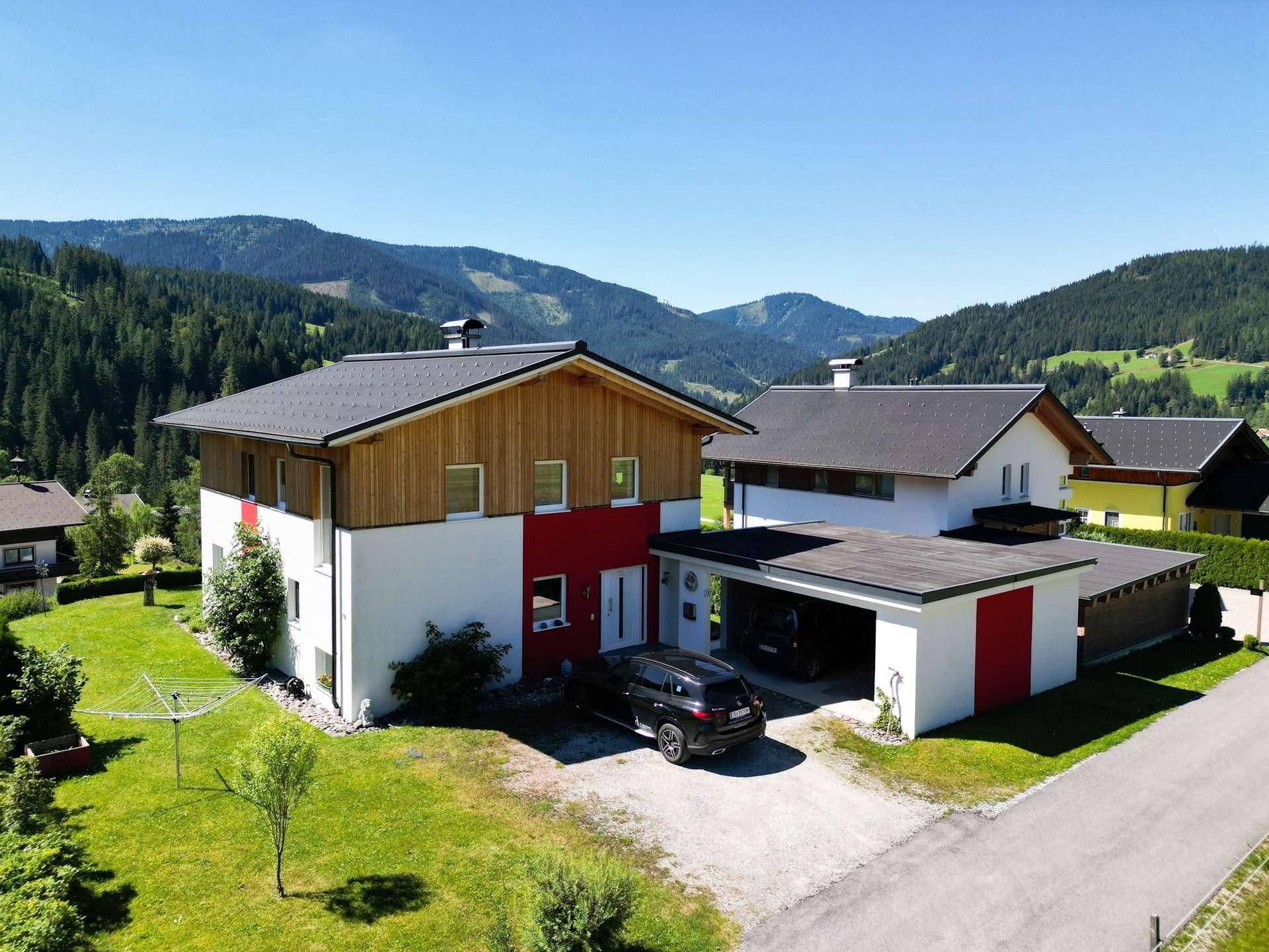 Das moderne Wohnhaus mit Carport und Garten, eingebettet in eine malerische Berglandschaft.