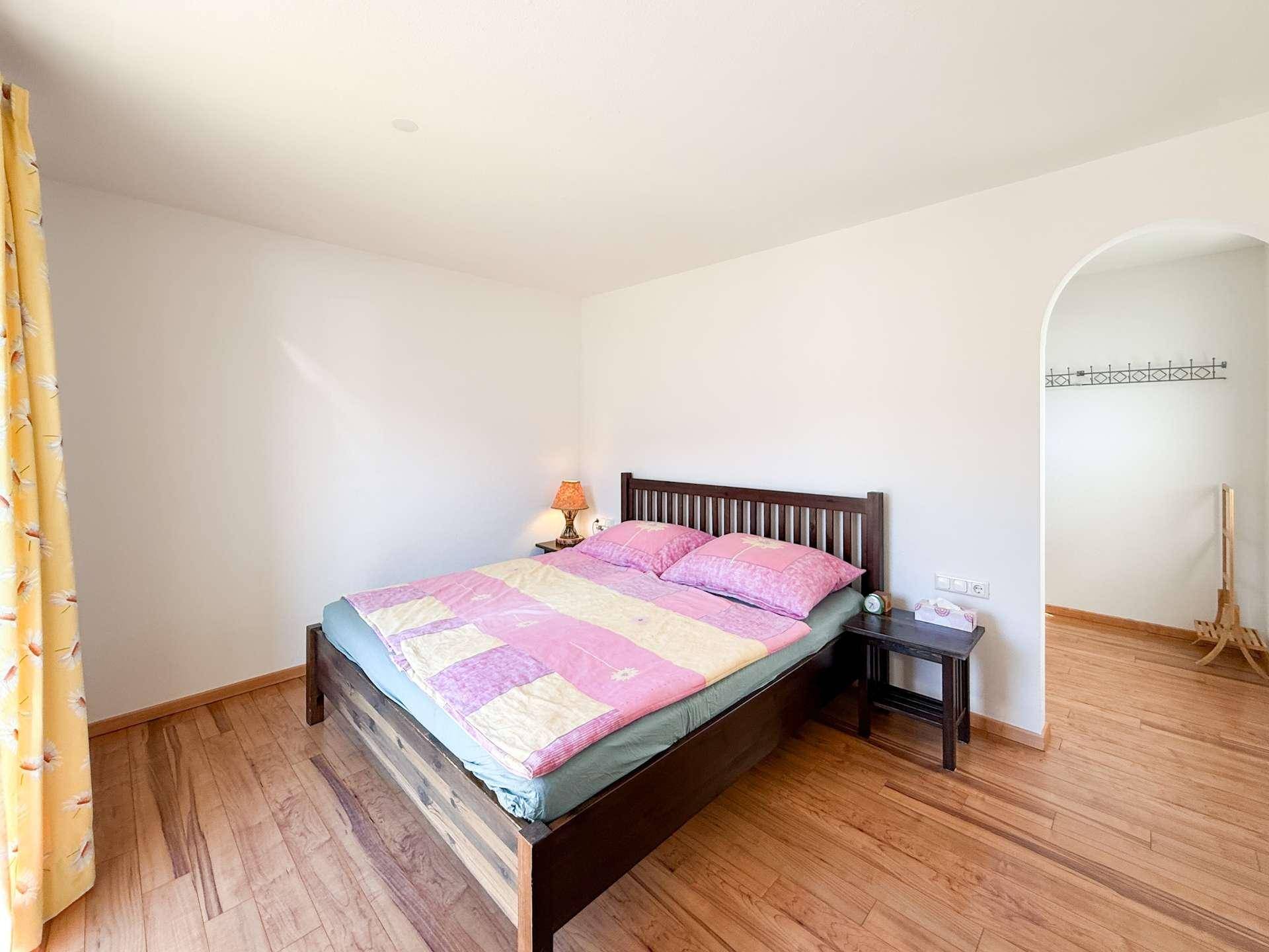 Schlafzimmer mit Doppelbett, Holzboden und einem offenen Durchgang zu einem Ankleidebereich.