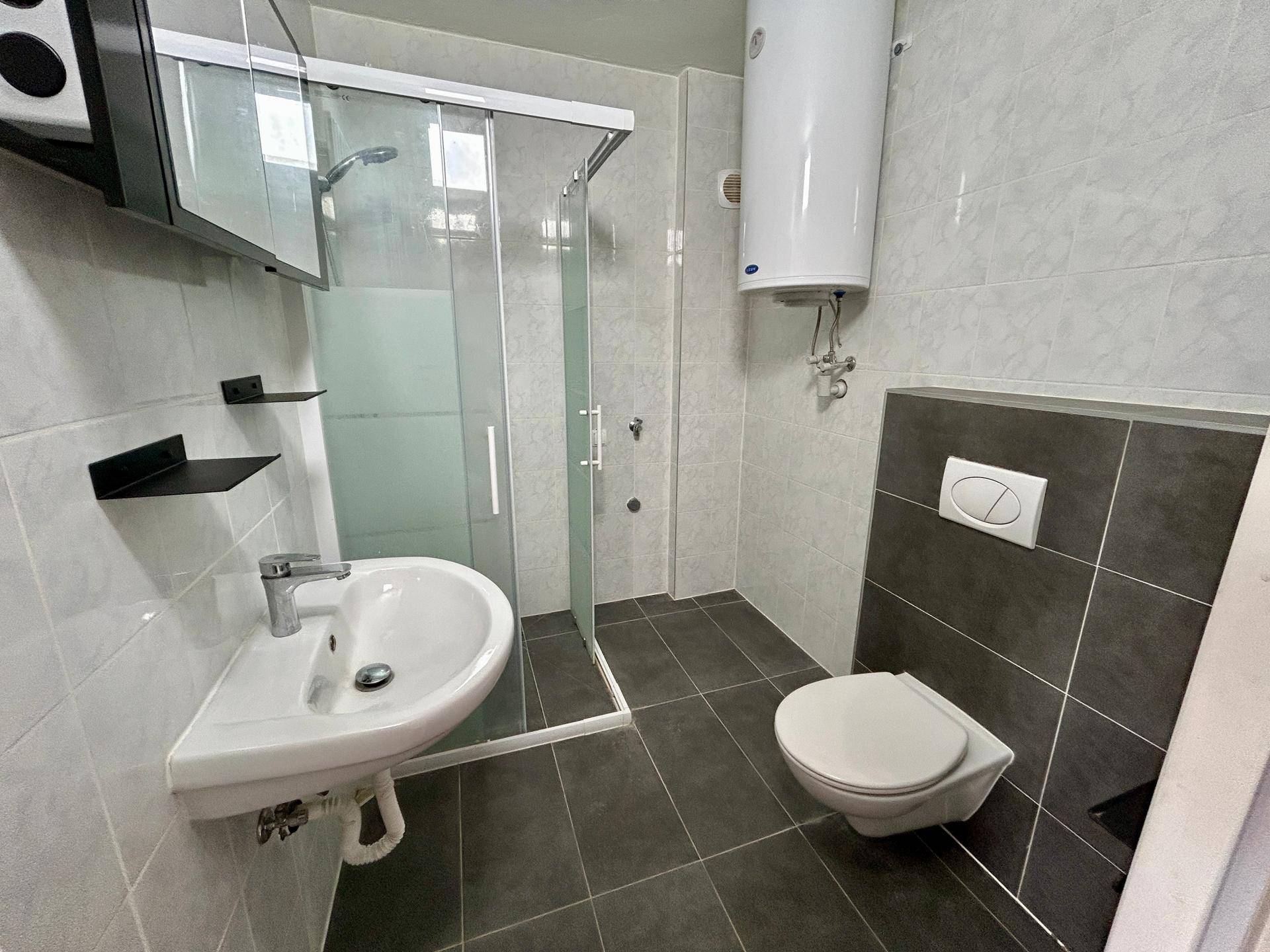 Modernes Badezimmer mit Duschkabine, wandhängendem WC und hellgrauen Fliesen.