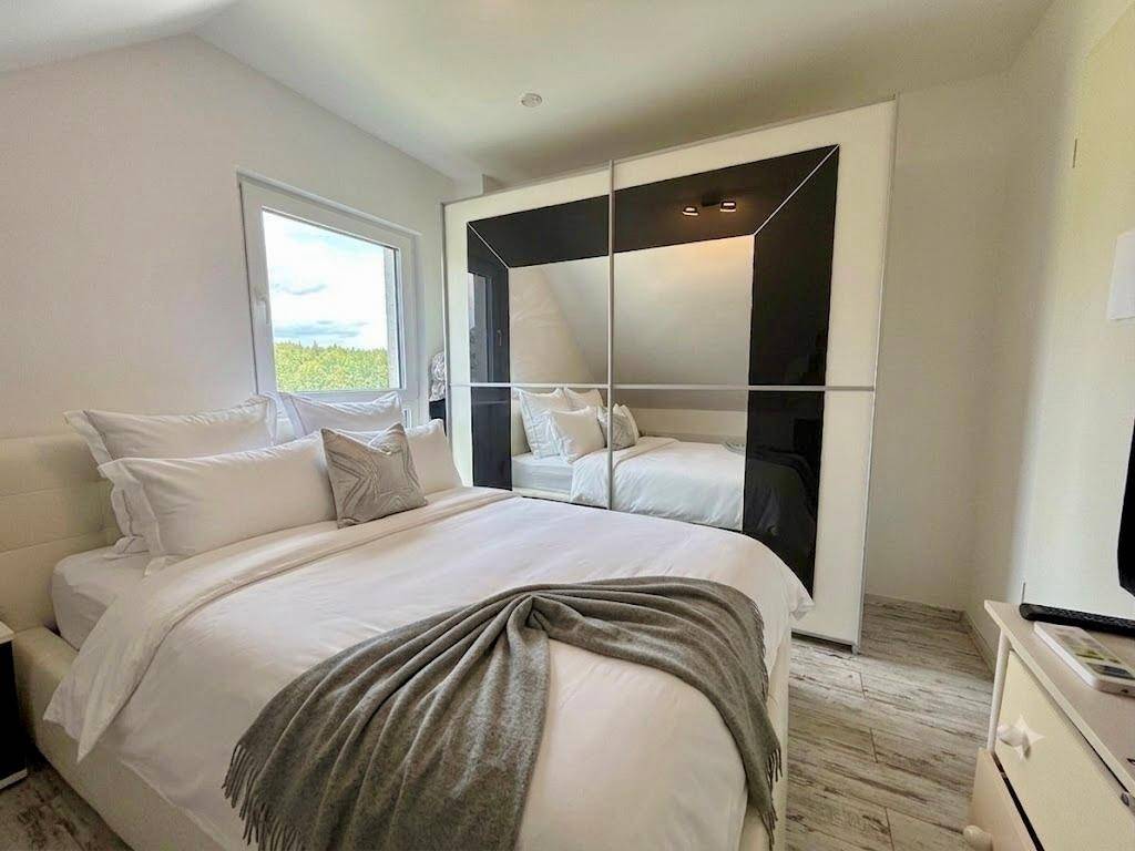 Helles Schlafzimmer mit großem Bett, Spiegelschrank und Blick ins Grüne.
