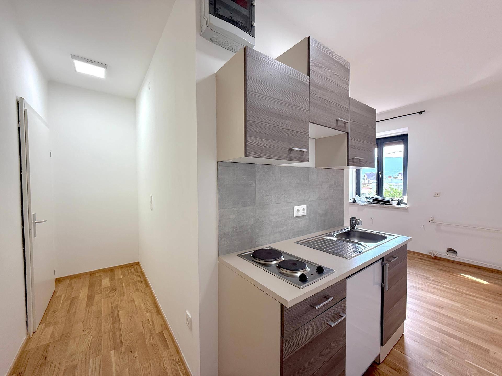 Kompakte Einbauküche mit Spüle, Kochfeld und Oberschränken in einem hellen Raum mit Fenster.