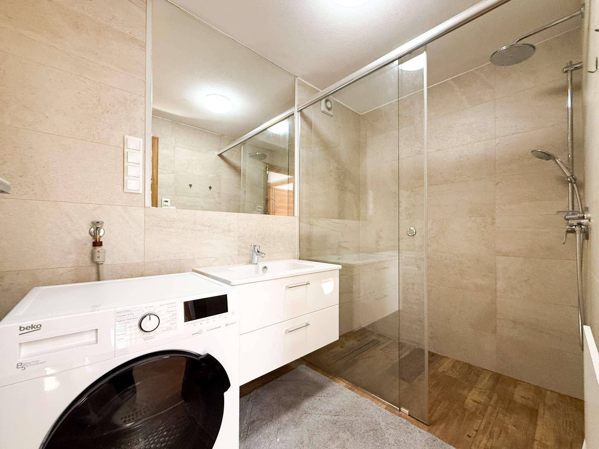 Modernes Badezimmer mit begehbarer Dusche, Waschtisch und integrierter Waschmaschine.