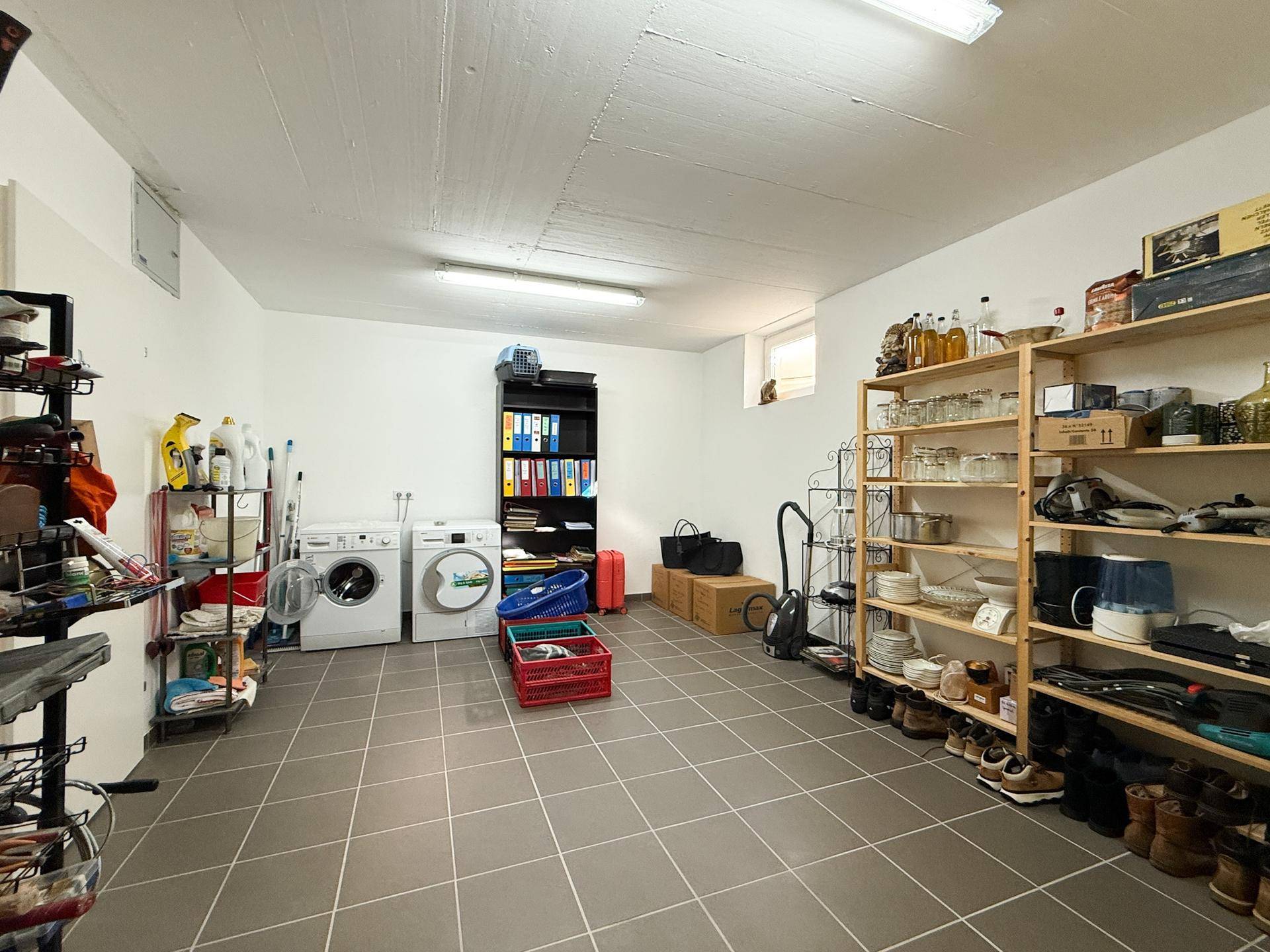 Geräumiger Hauswirtschaftsraum mit Waschmaschinen, Regalen und Fliesenboden, ideal als Abstellraum.