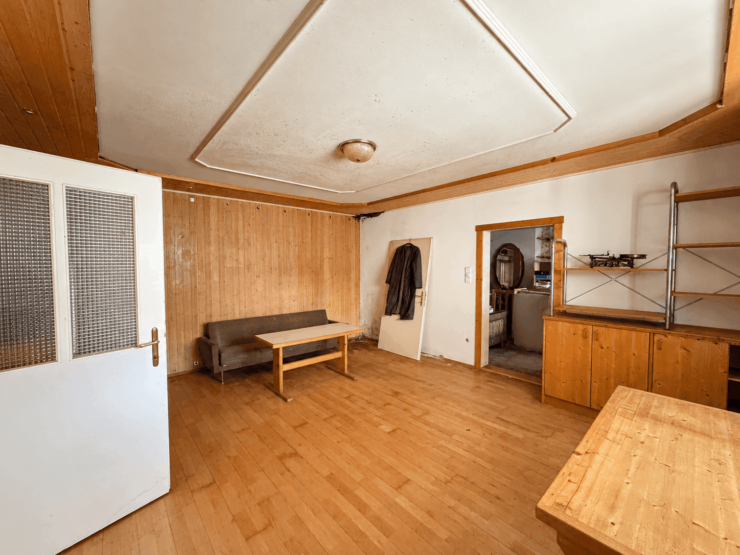 Geräumiges Wohnzimmer mit Holzpaneelen, Holzboden und Zugang zu weiteren Räumen.