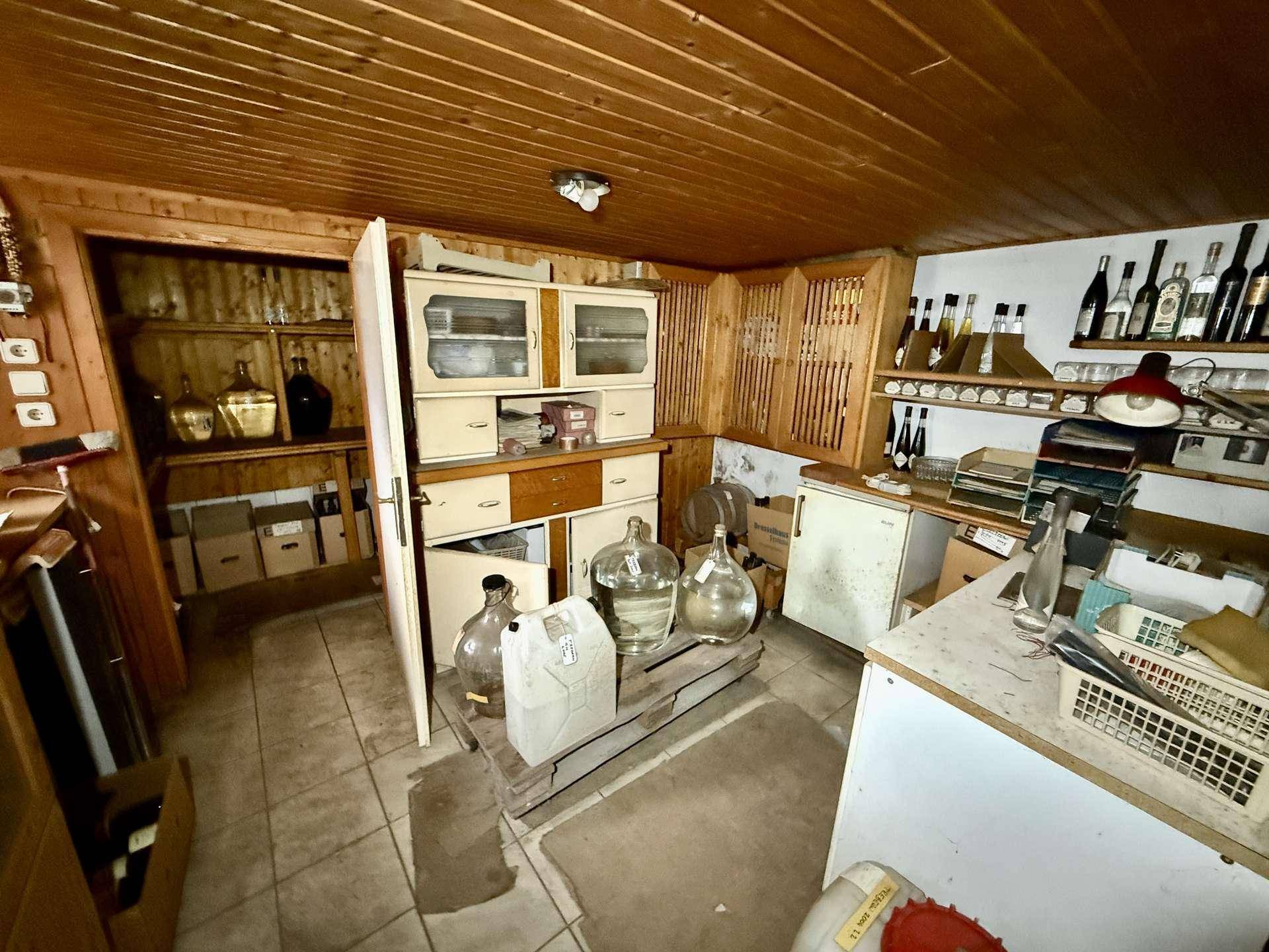 Lagerraum oder Keller mit Holzdecke, Fliesenboden und Regalen für Vorräte und Flaschen.