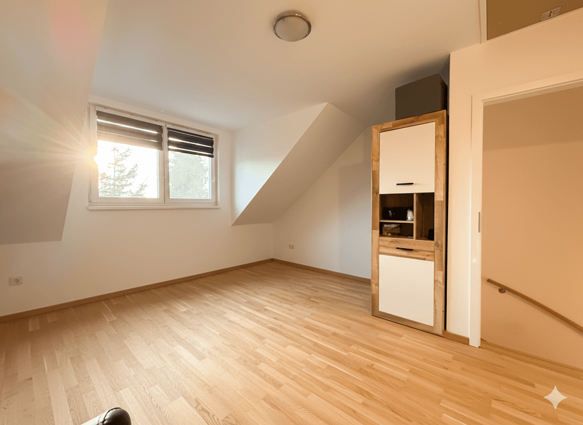 Helles, leeres Zimmer mit Holzboden, Dachschräge und Fenster mit viel Tageslicht.