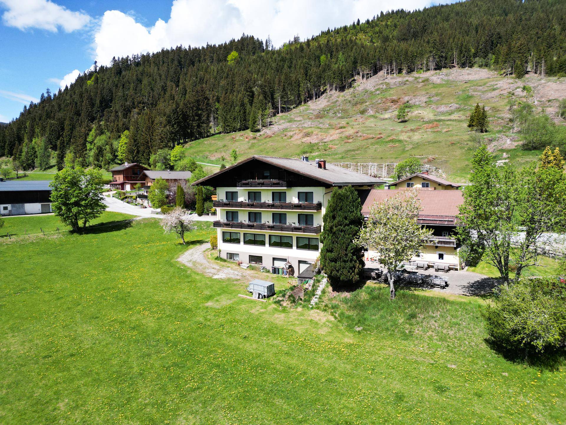 Ansicht eines traditionellen Gebäudes mit Holzbalkonen, eingebettet in eine grüne Hügellandschaft mit Wald.