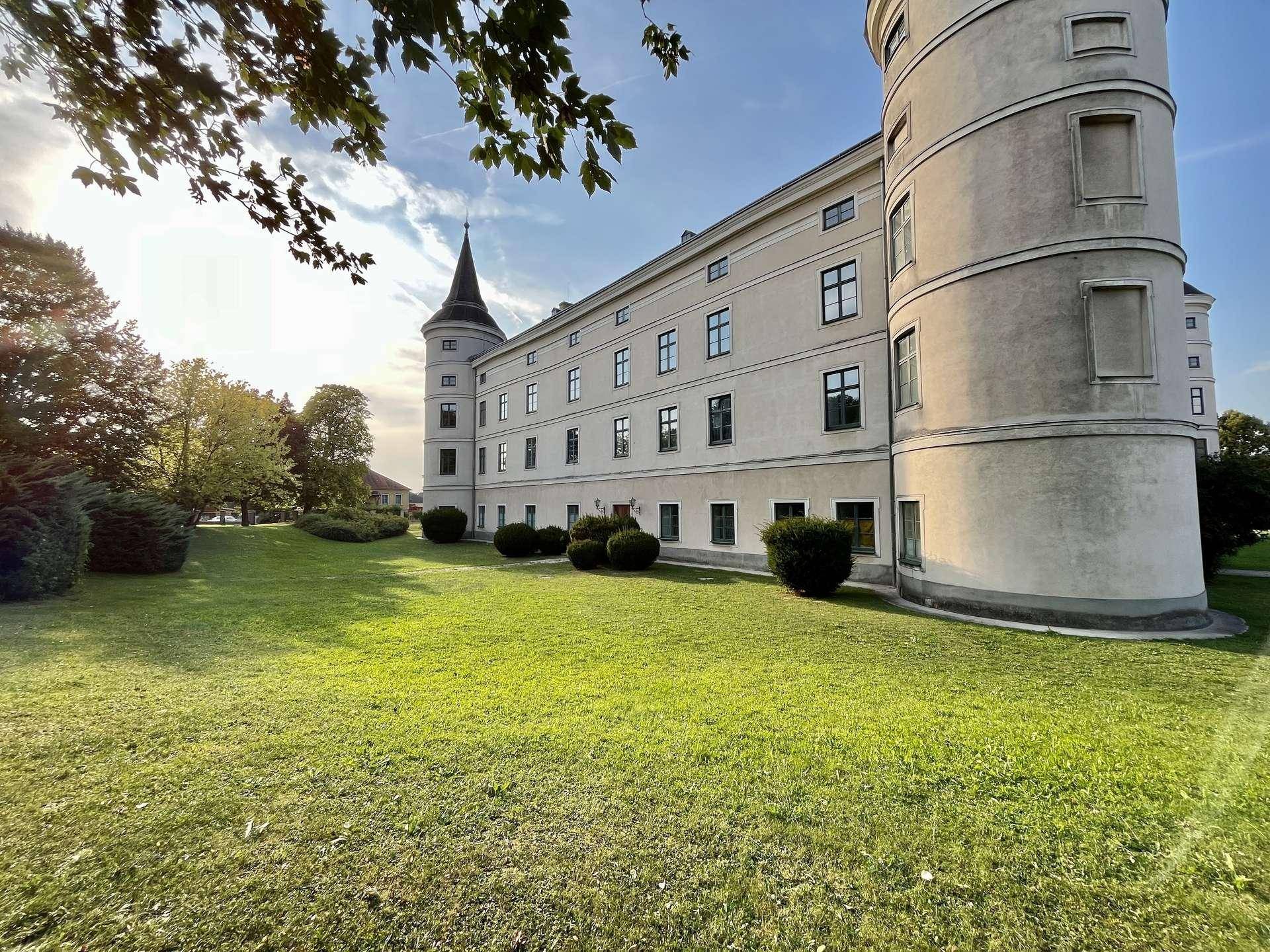 Historisches Gebäude mit Türmen und weitläufigen Grünflächen unter strahlend blauem Himmel.