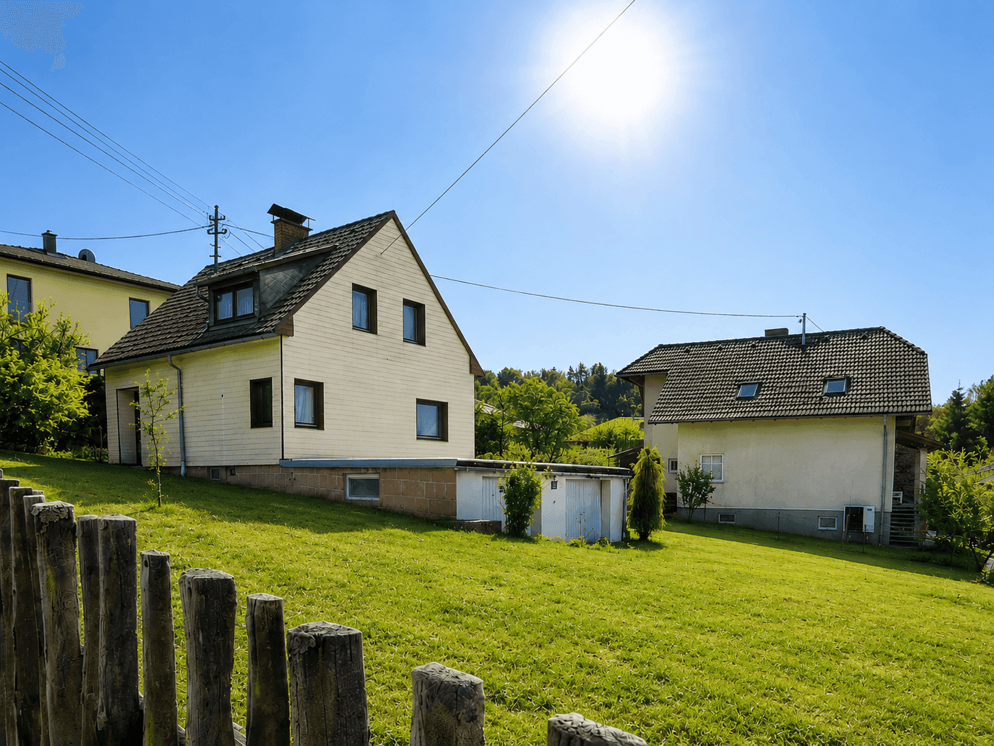 Seitenansicht des Hauses mit Garten, Schuppen und Holzzaun unter strahlendem Sonnenschein.