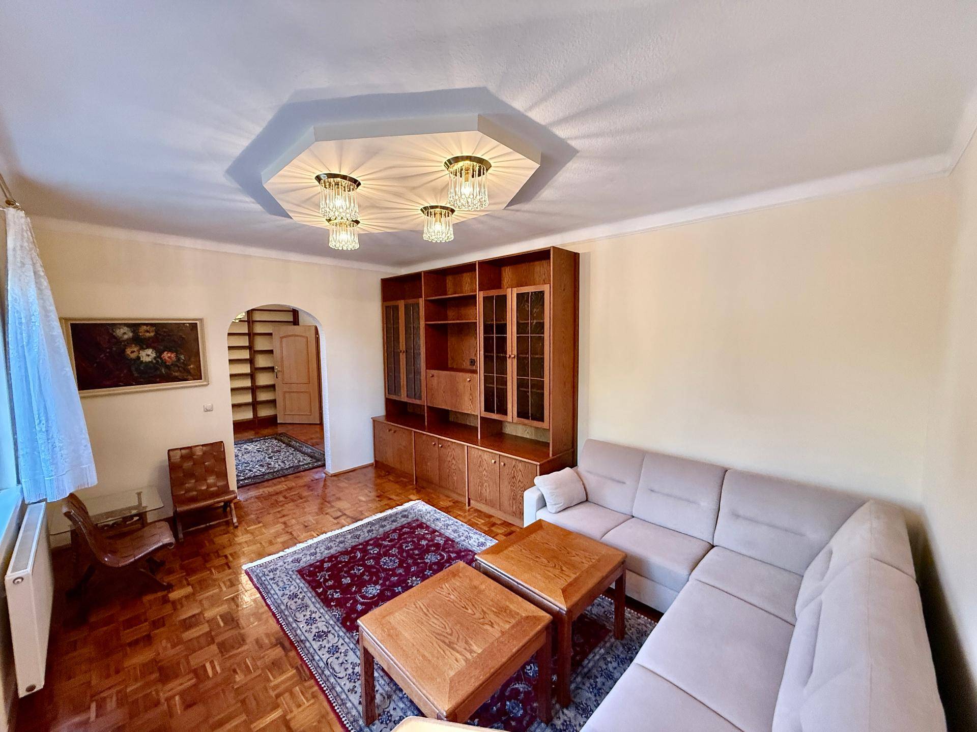 Gemütliches Wohnzimmer mit Parkettboden, beiger Eckcouch und traditionellen Holzmöbeln.