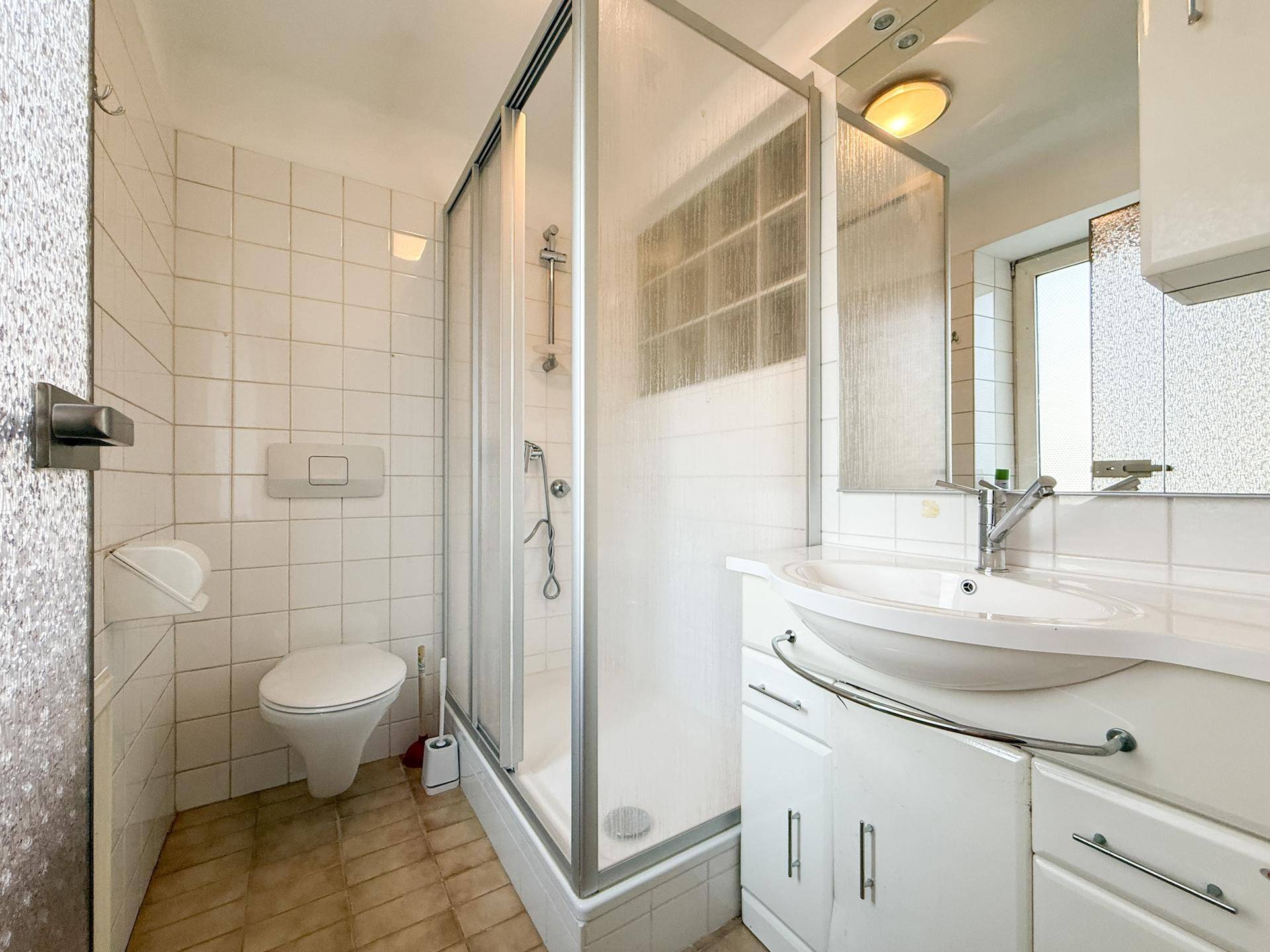 Badezimmer mit Dusche, WC, Waschbecken und weißen Fliesen.