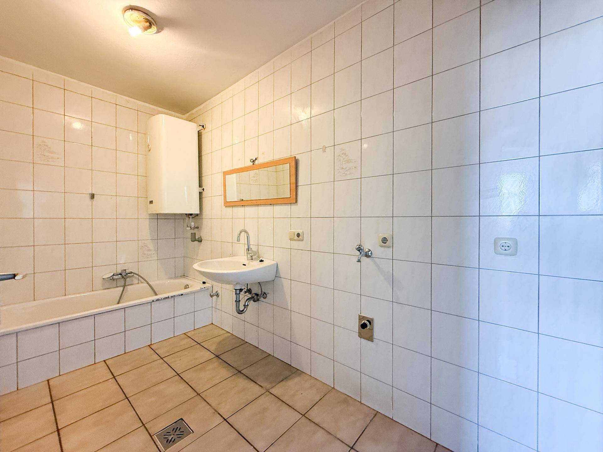 Gefliestes Badezimmer mit Badewanne, Waschbecken und Boiler, bereit zur Modernisierung.