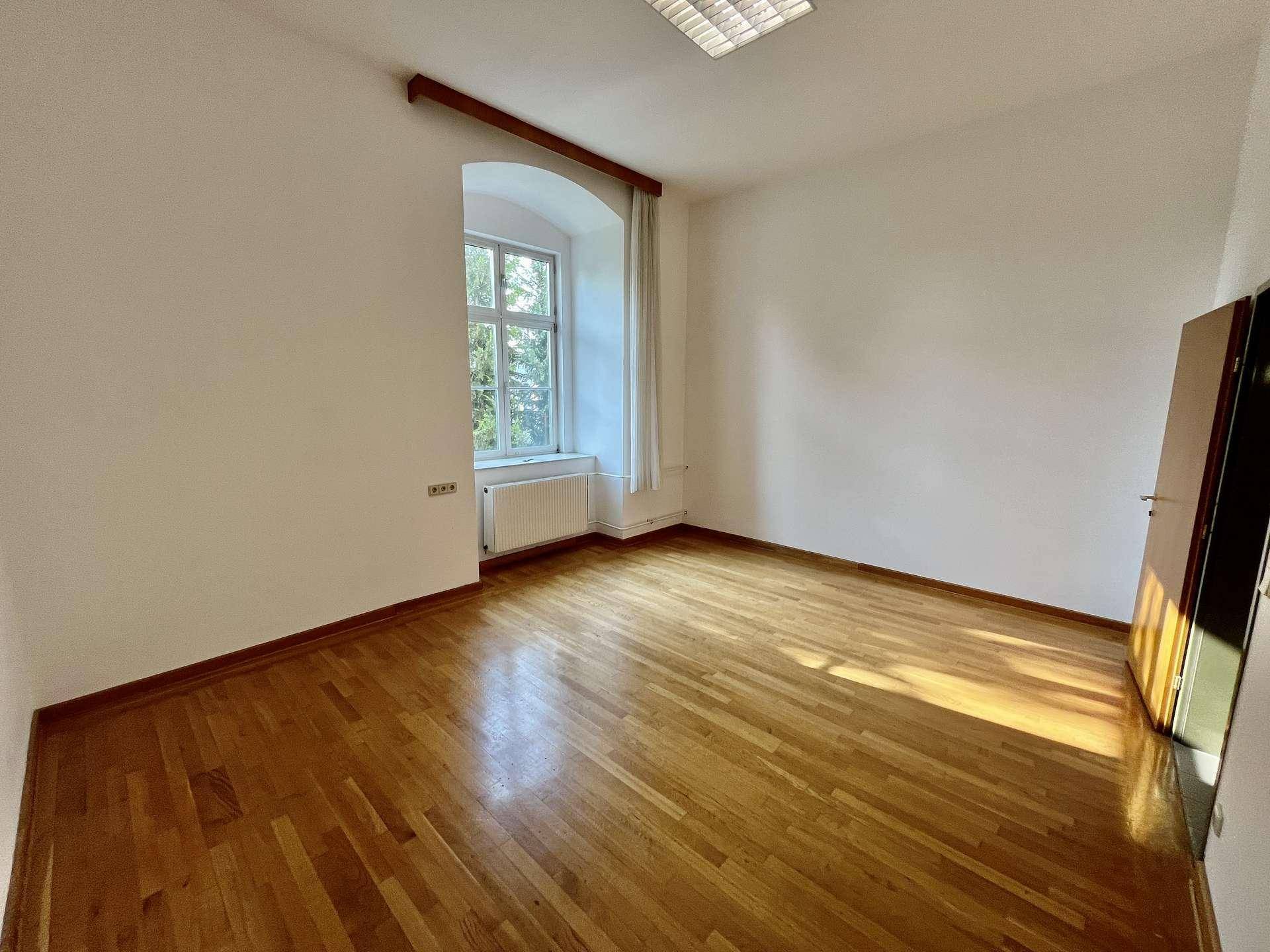 Kleinerer Büroraum mit Holzboden, einem Fenster und einer Holztür, die den Eingang bildet.