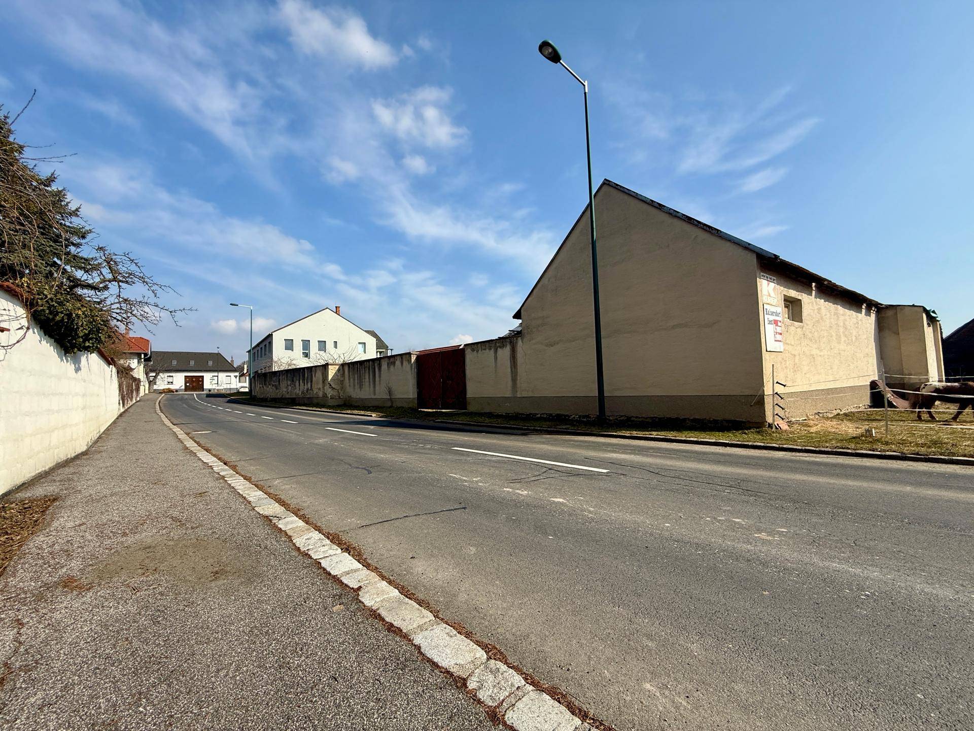 Seitenansicht eines Gebäudes an einer Straße mit angrenzender Mauer.