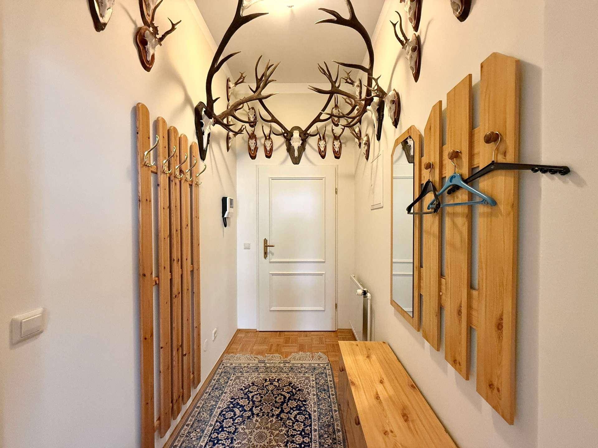 Traditioneller Flur mit Holzelementen, Garderobe und zahlreichen Hirschgeweihen als Dekoration.