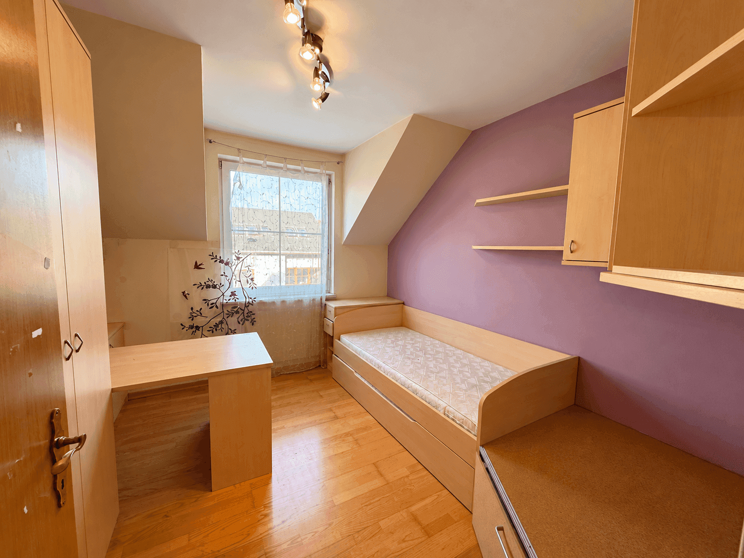Helles Schlafzimmer mit Einzelbett, Schreibtisch und lila Wandakzenten unter Dachschräge.