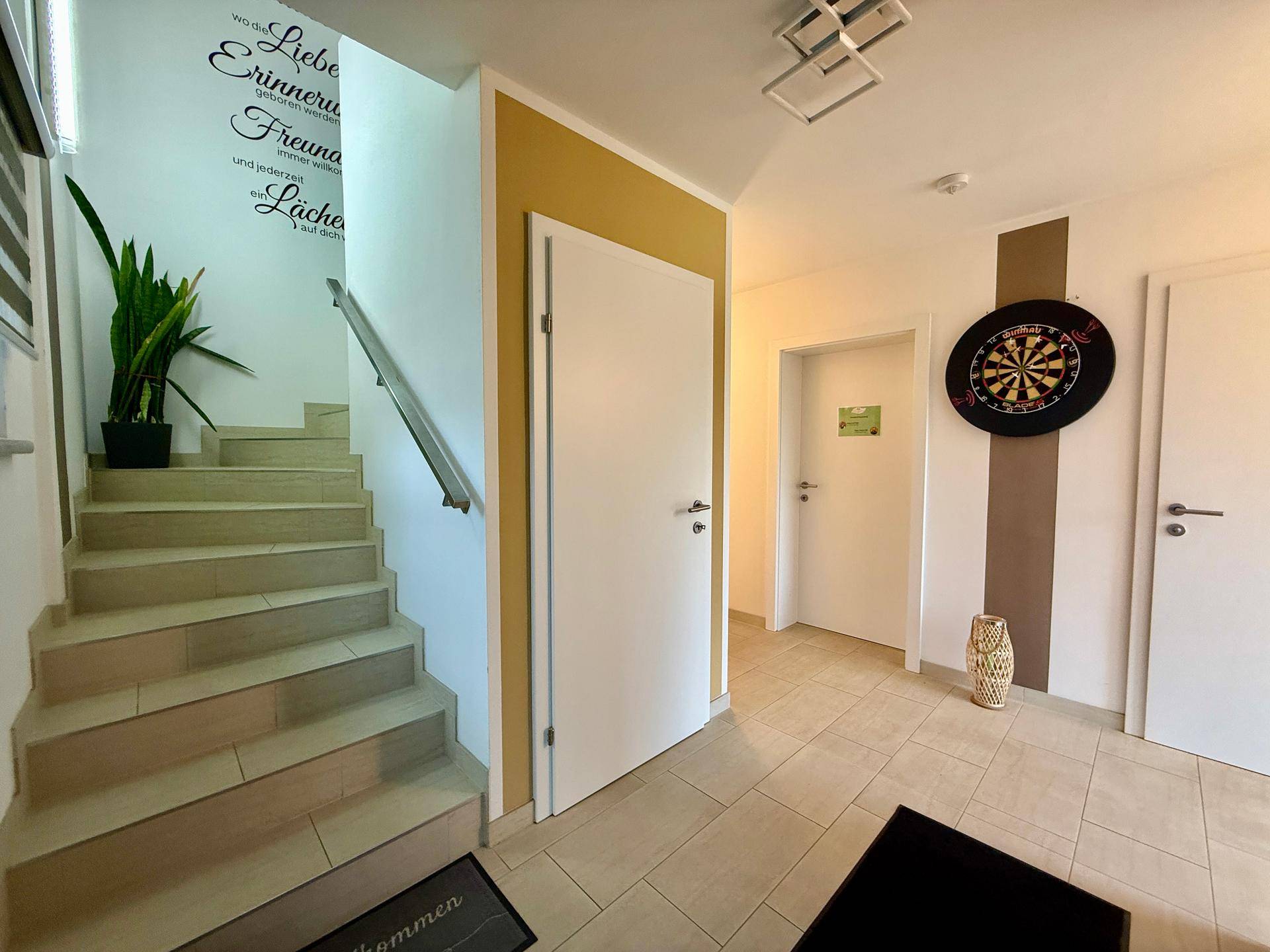 Heller Flur mit Treppe, Fliesenboden und einer Dartscheibe an der Wand.