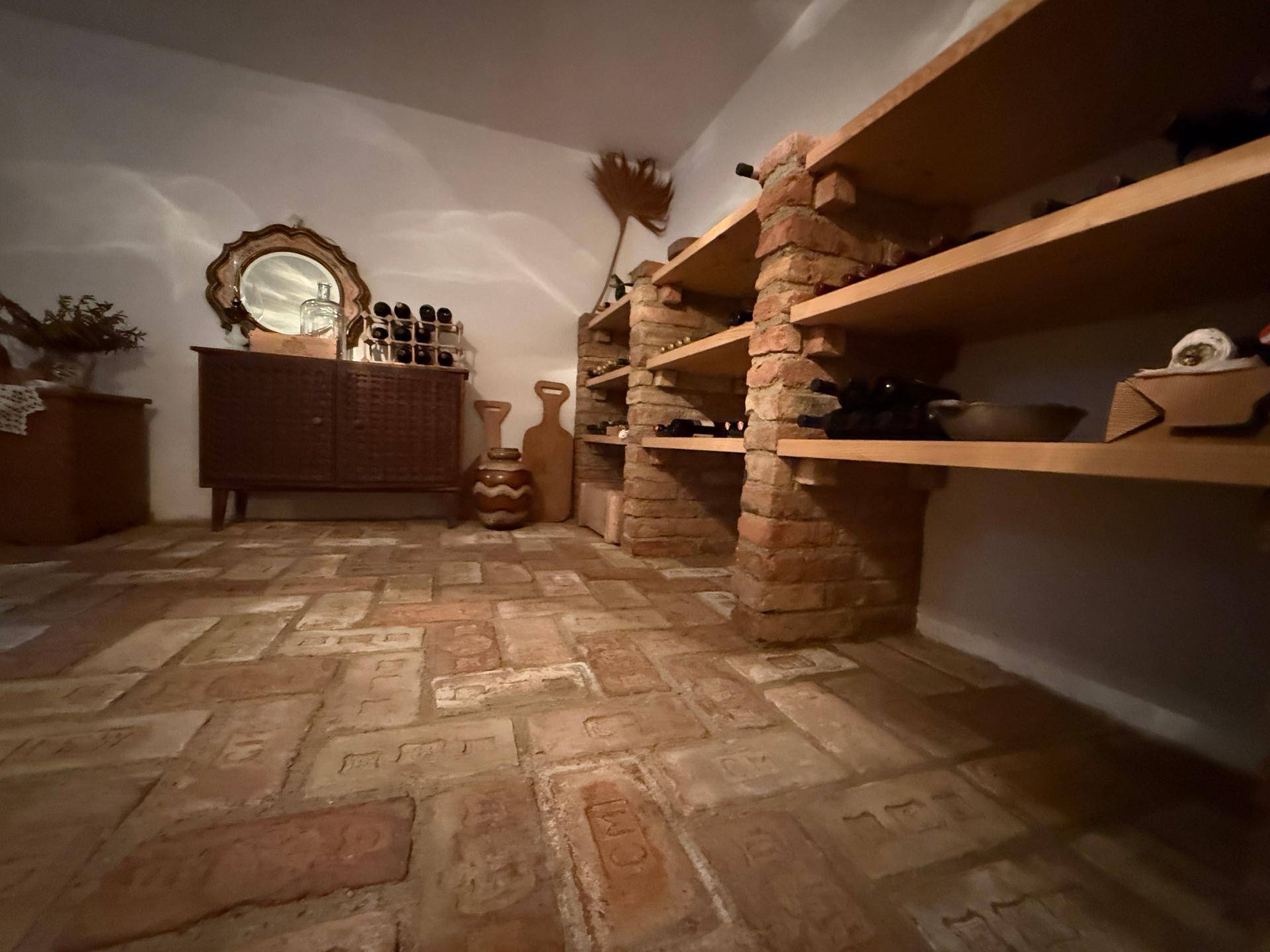 Rustikaler Weinkeller mit Ziegelboden und Holzregalen zur Weinlagerung.