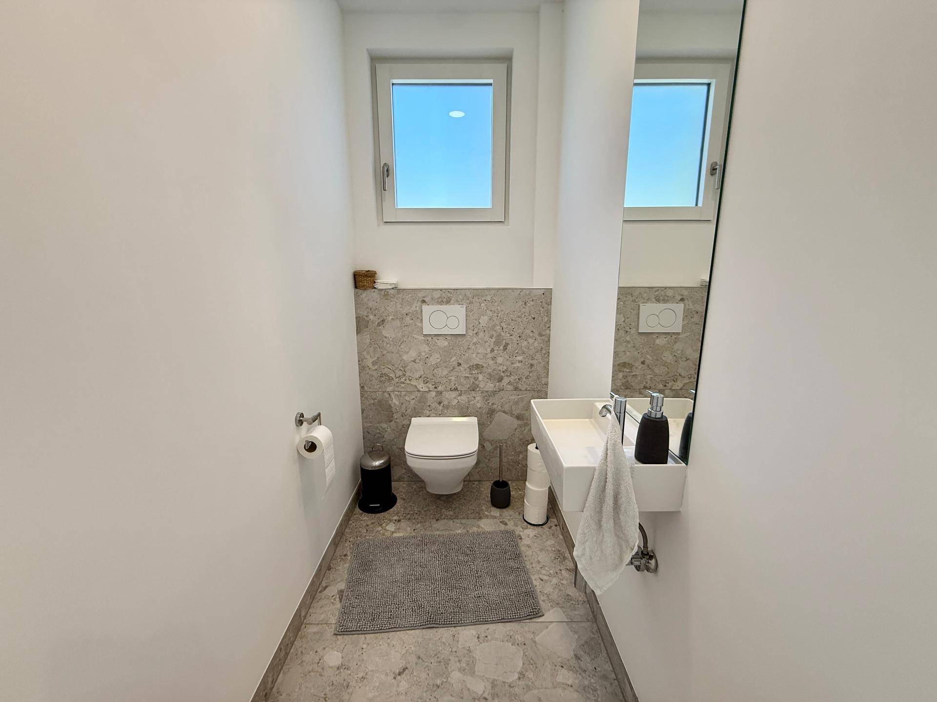 Modernes Gäste-WC mit Fenster, Wand-WC und kleinem Waschbecken.