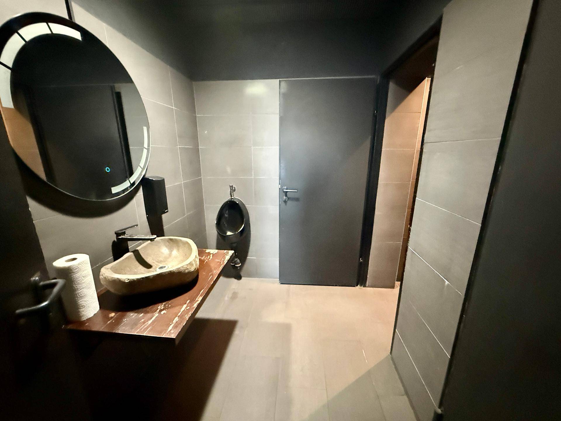 Zeitgemäßes Badezimmer mit Urinal, Steinswaschbecken und grauen Fliesen.