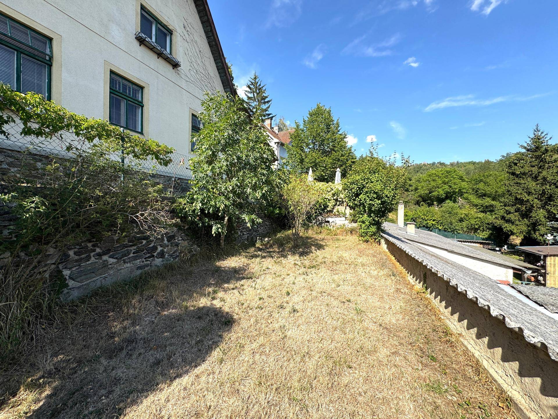 Großer Gartenbereich mit trockenem Rasen, Bäumen und Blick auf die umliegende Landschaft.